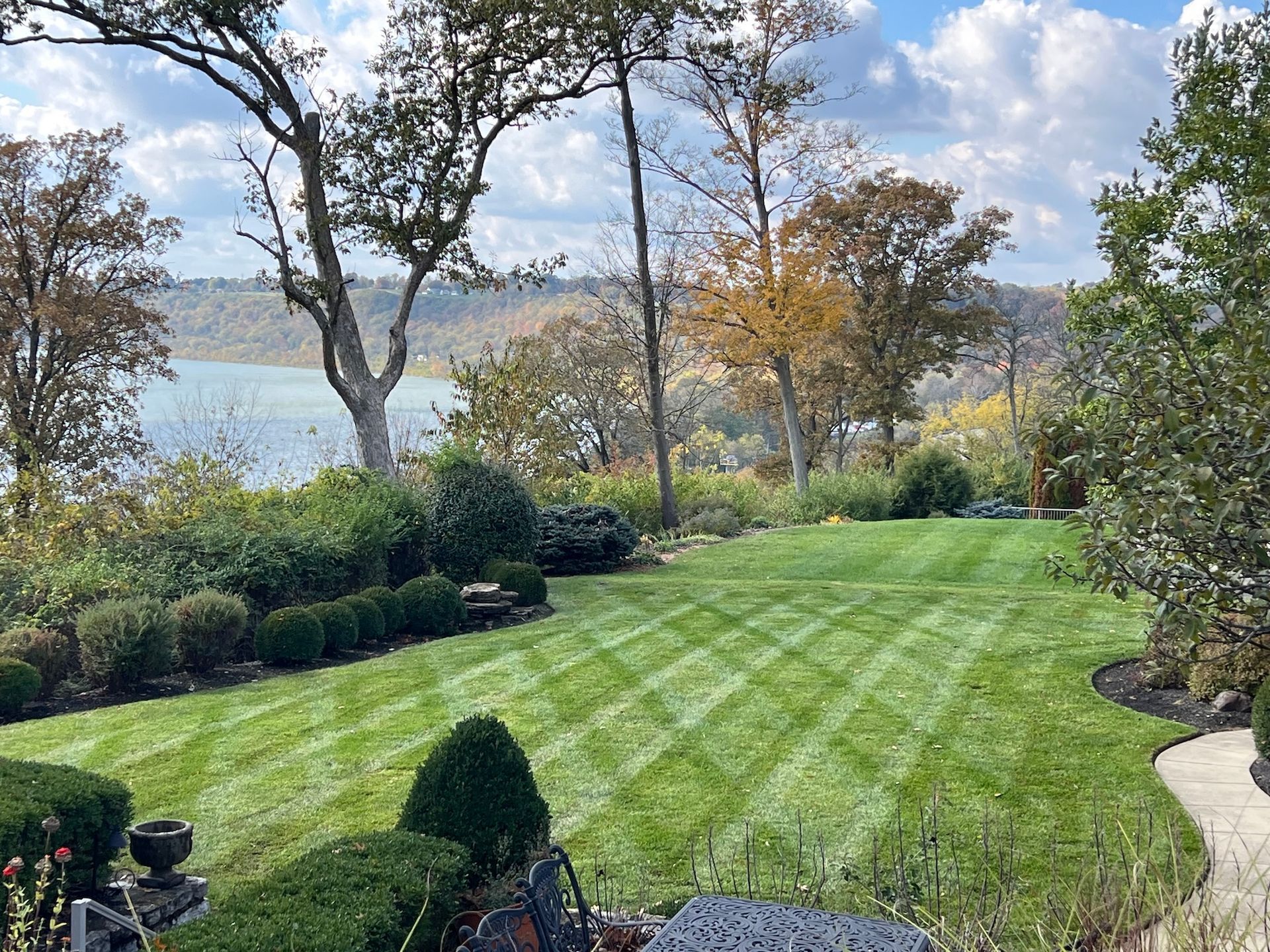 Lawn with striped pattern overlooking a body of water and trees on a partly cloudy day.