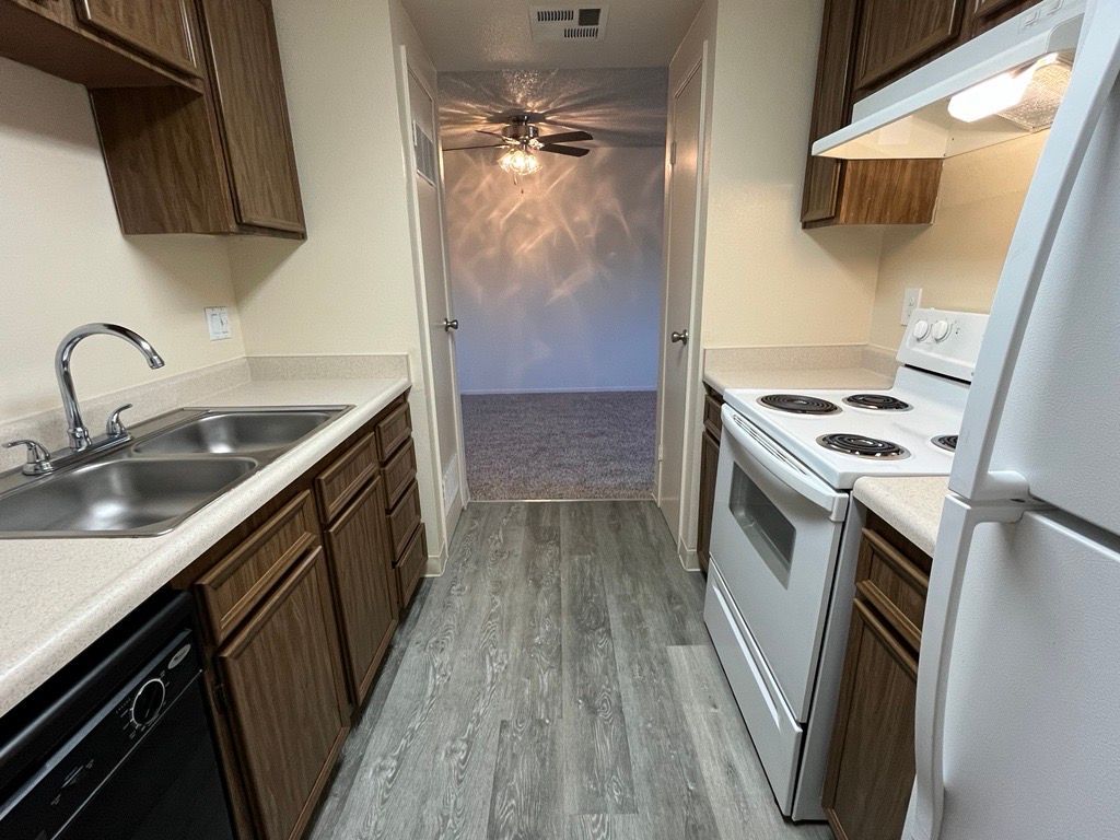 Kitchen with dark cabinets, white appliances, and a gray floor, looking into an adjacent room.