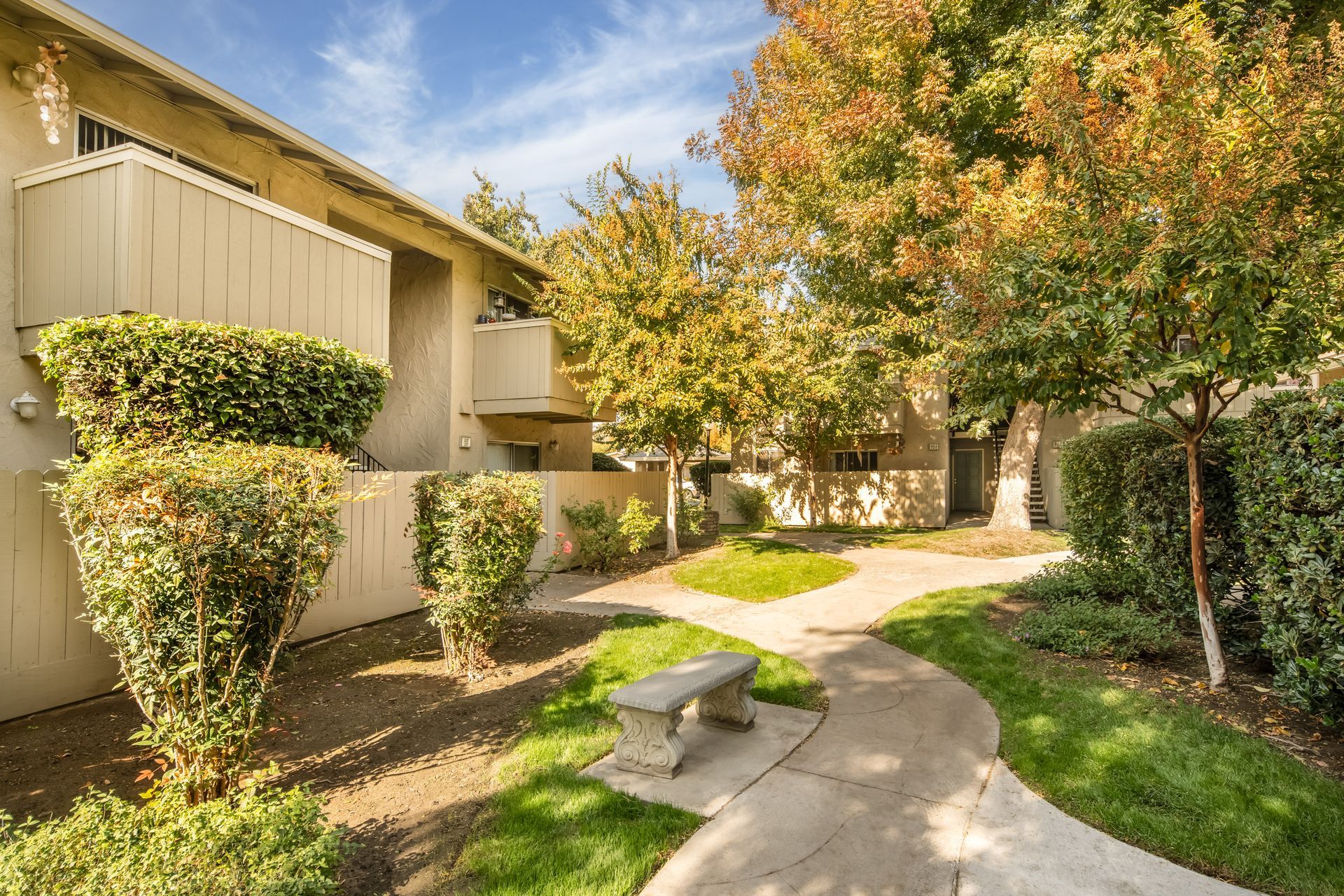 Courtyard with a stone bench, pathway, trees, and beige apartment buildings.