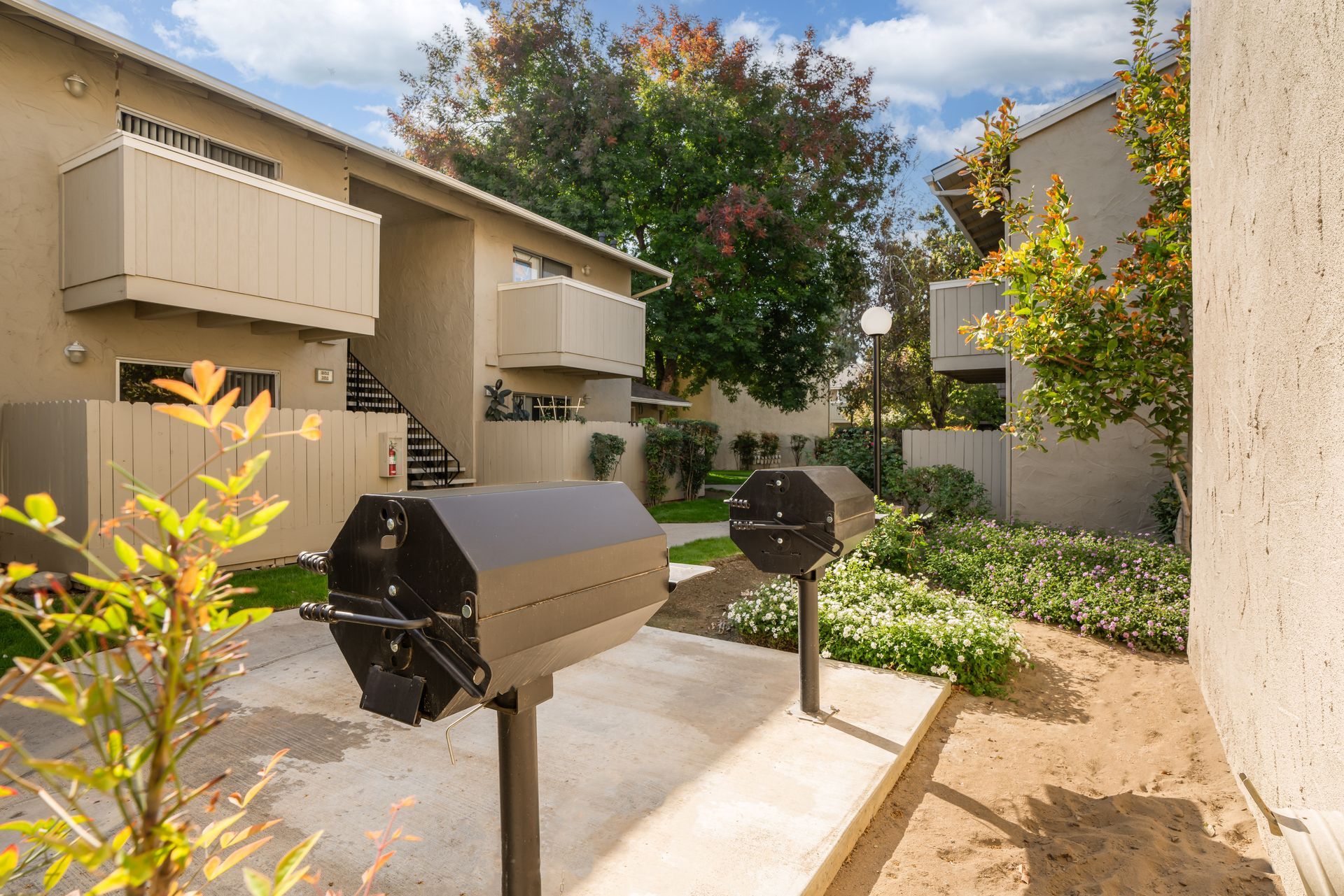 Apartment complex with barbecue grills in a common area, surrounded by landscaping.