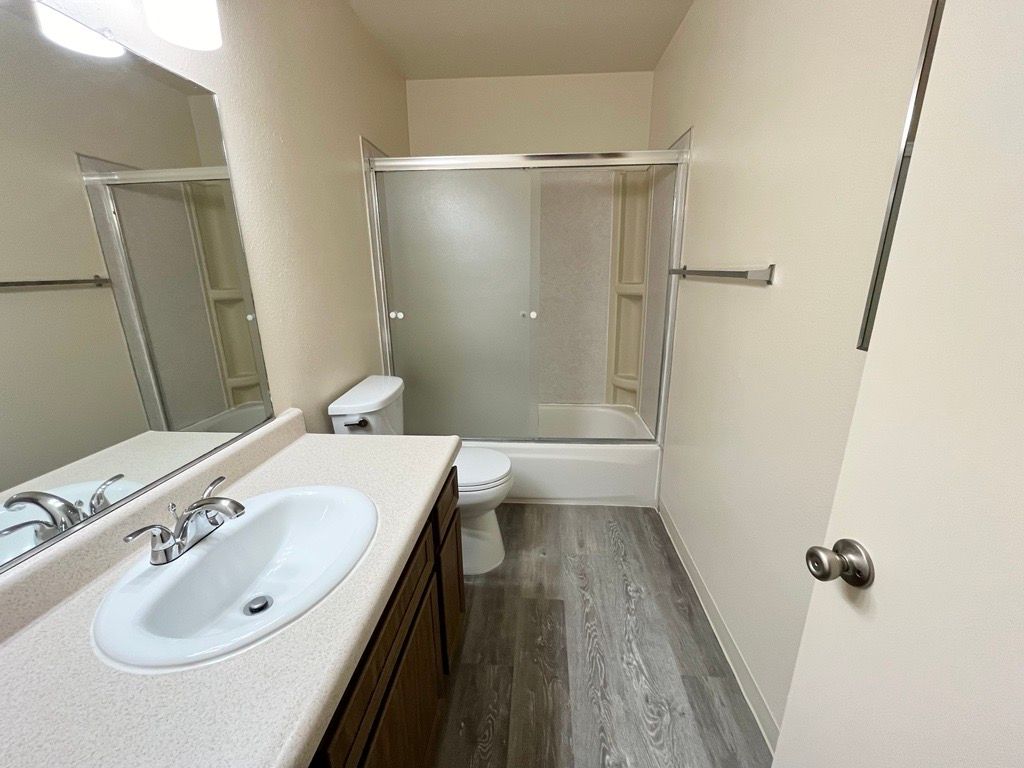 Bathroom with a white sink, toilet, and bathtub. Gray-brown flooring, light walls.