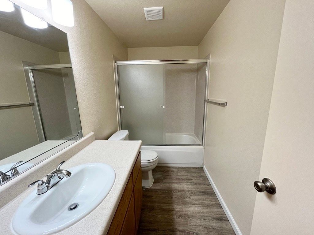 Bathroom with sink, toilet, shower/tub, and wood-look flooring; neutral tones.