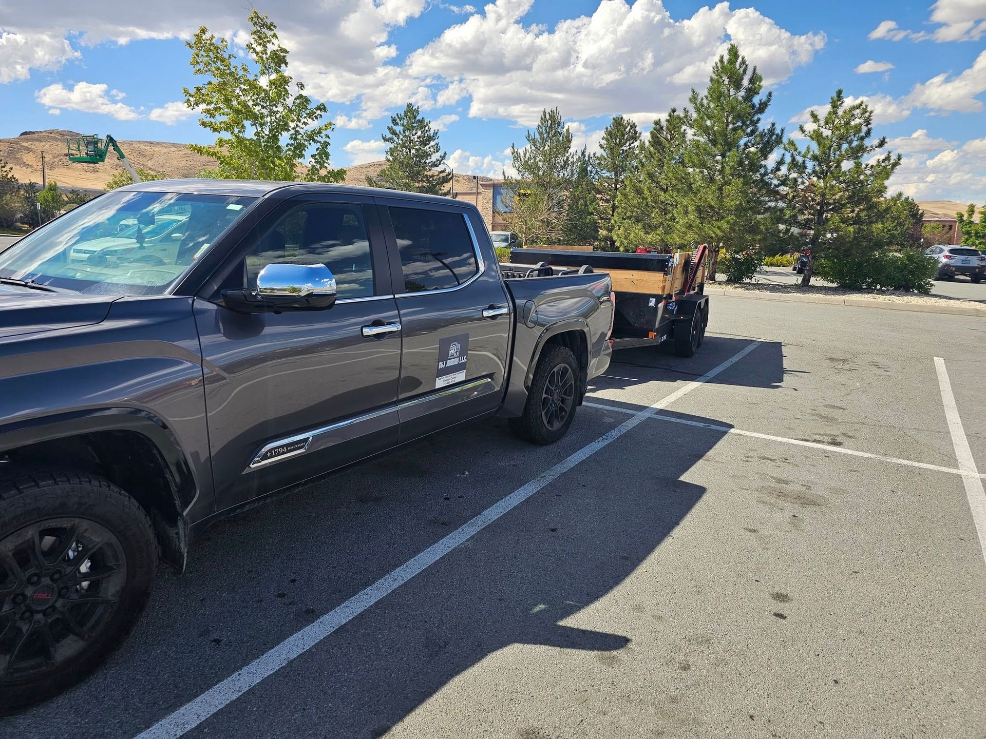 A dark gray pickup truck with a trailer parked in a parking lot on a sunny day.