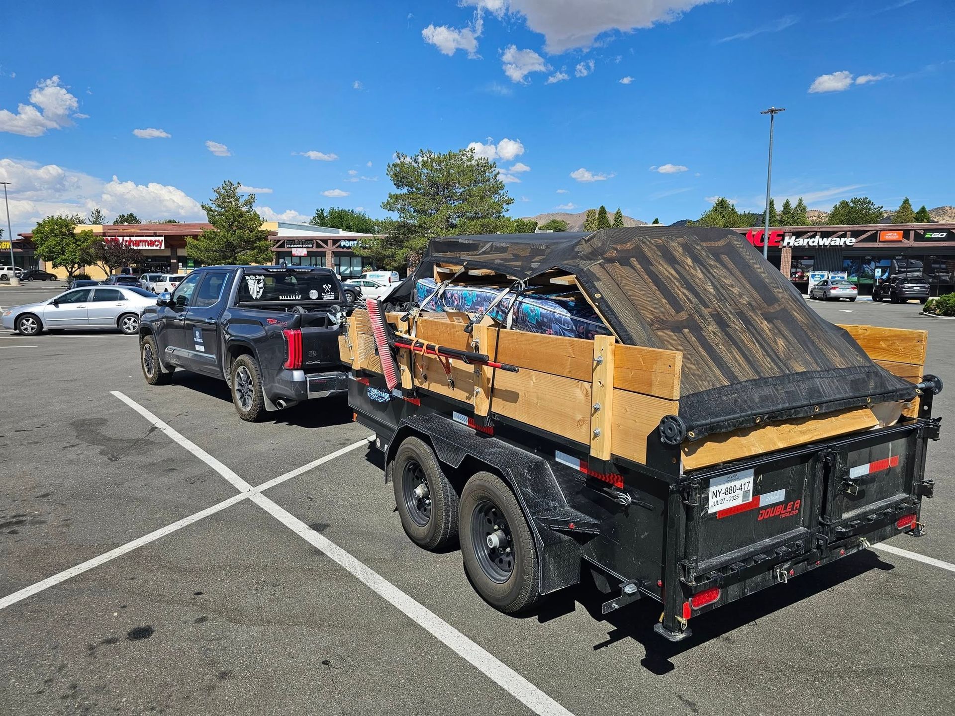 Black truck towing a trailer loaded with cardboard boxes and covered with a tarp in a parking lot on a sunny day.