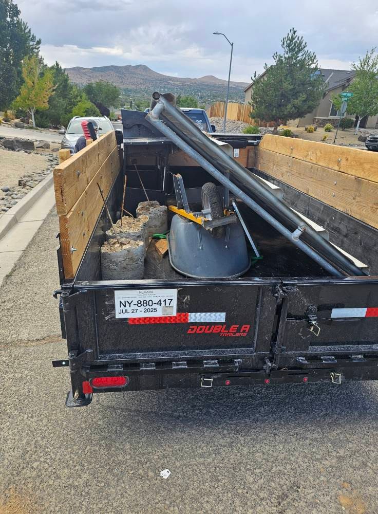 A black trailer loaded with construction debris and metal beams parked on a street. The trailer has wooden sideboards.