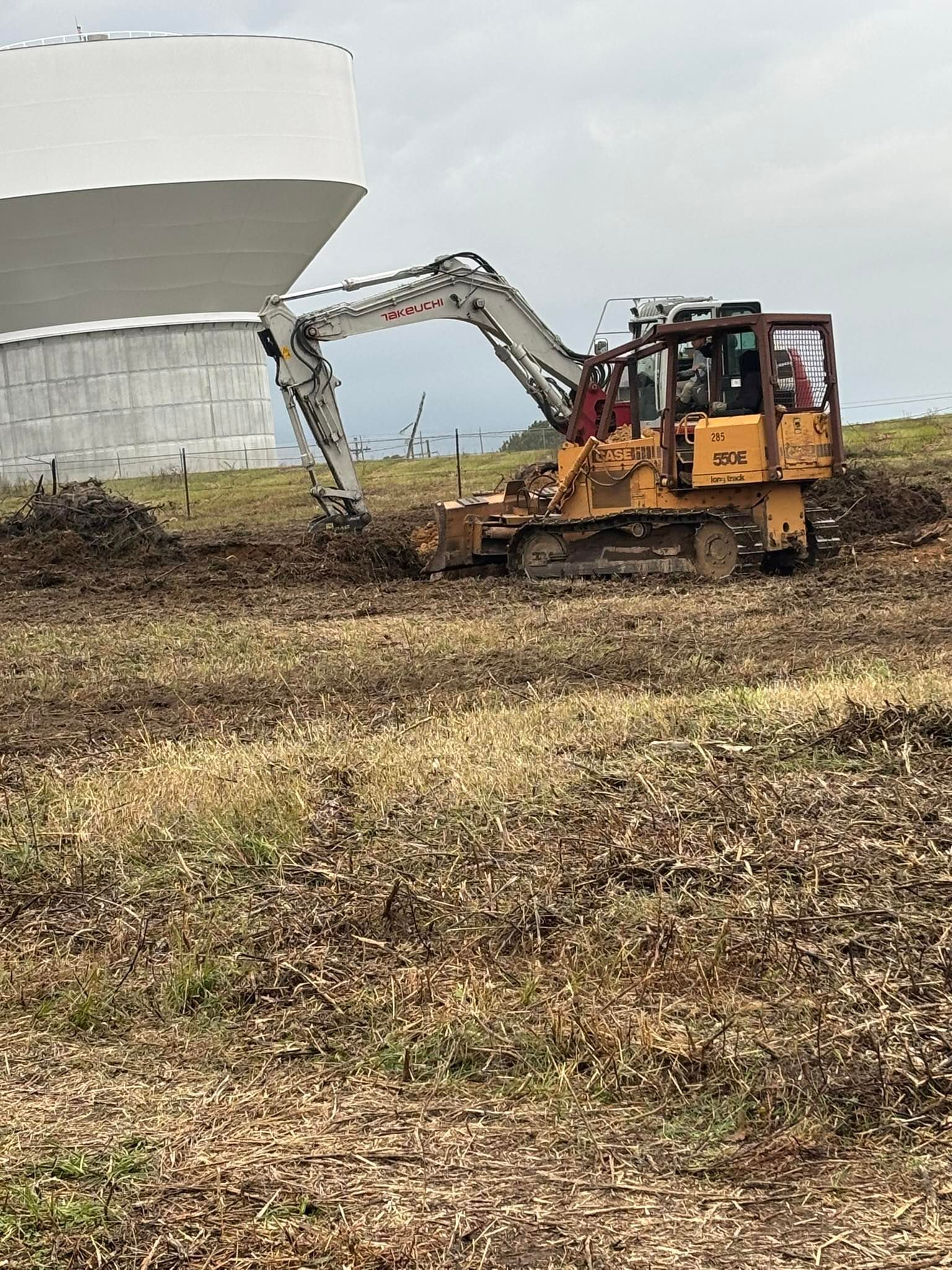 Yellow bulldozer clearing vegetation near a white modern building.