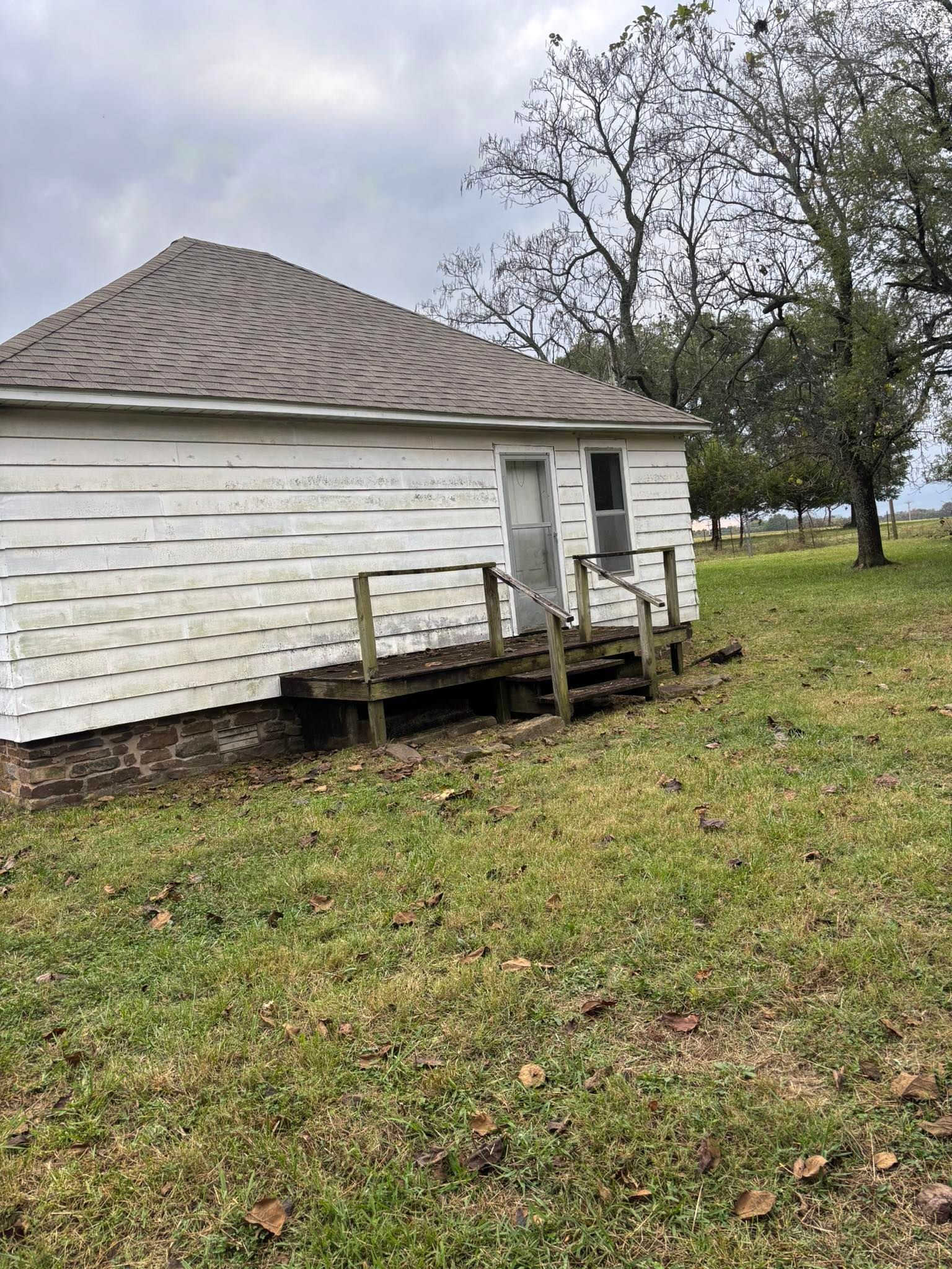 White building with a small wooden porch and steps, on a grassy field, under an overcast sky.