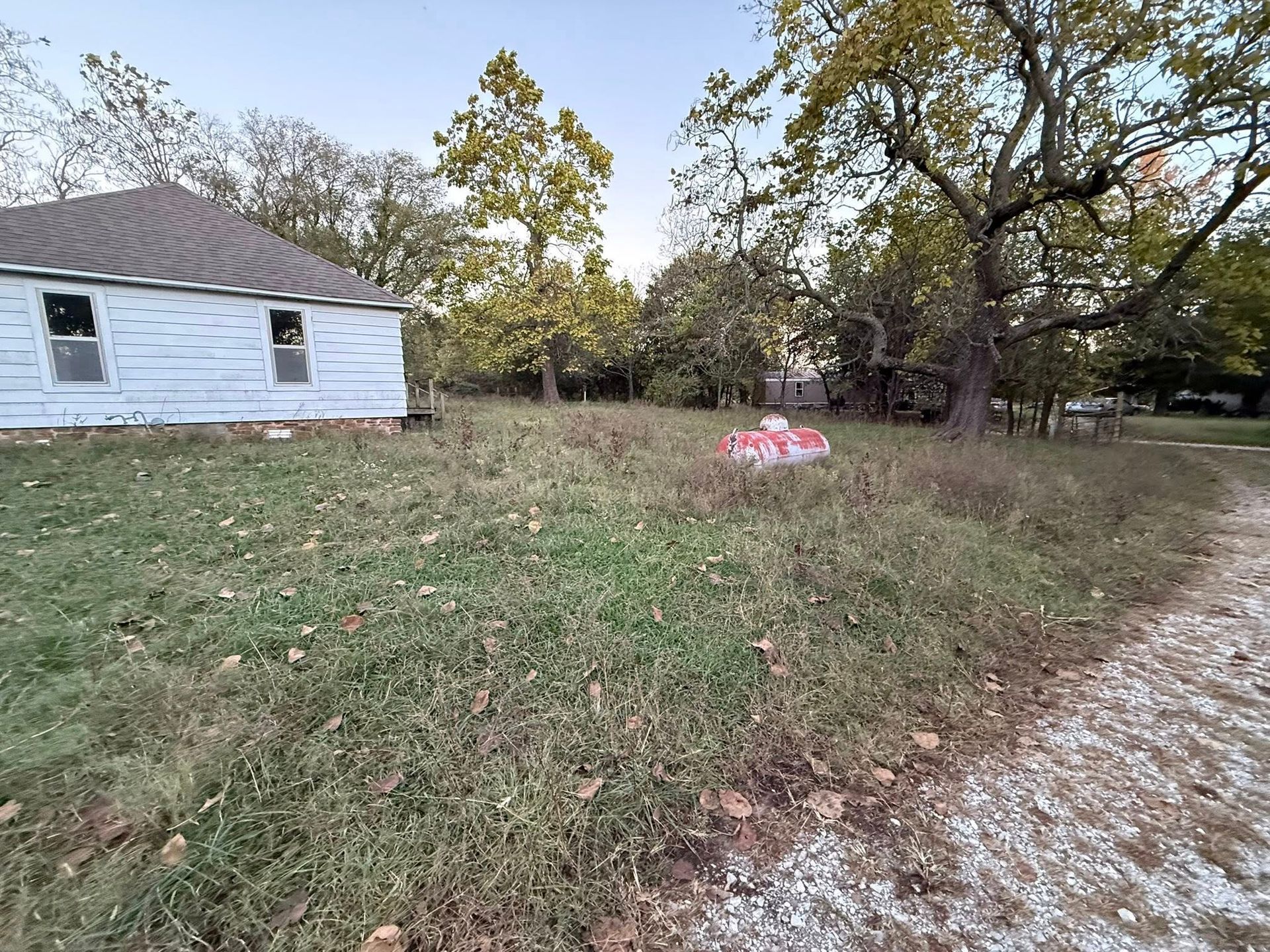 A small white house sits on a grassy hill; trees and a gravel road are visible.