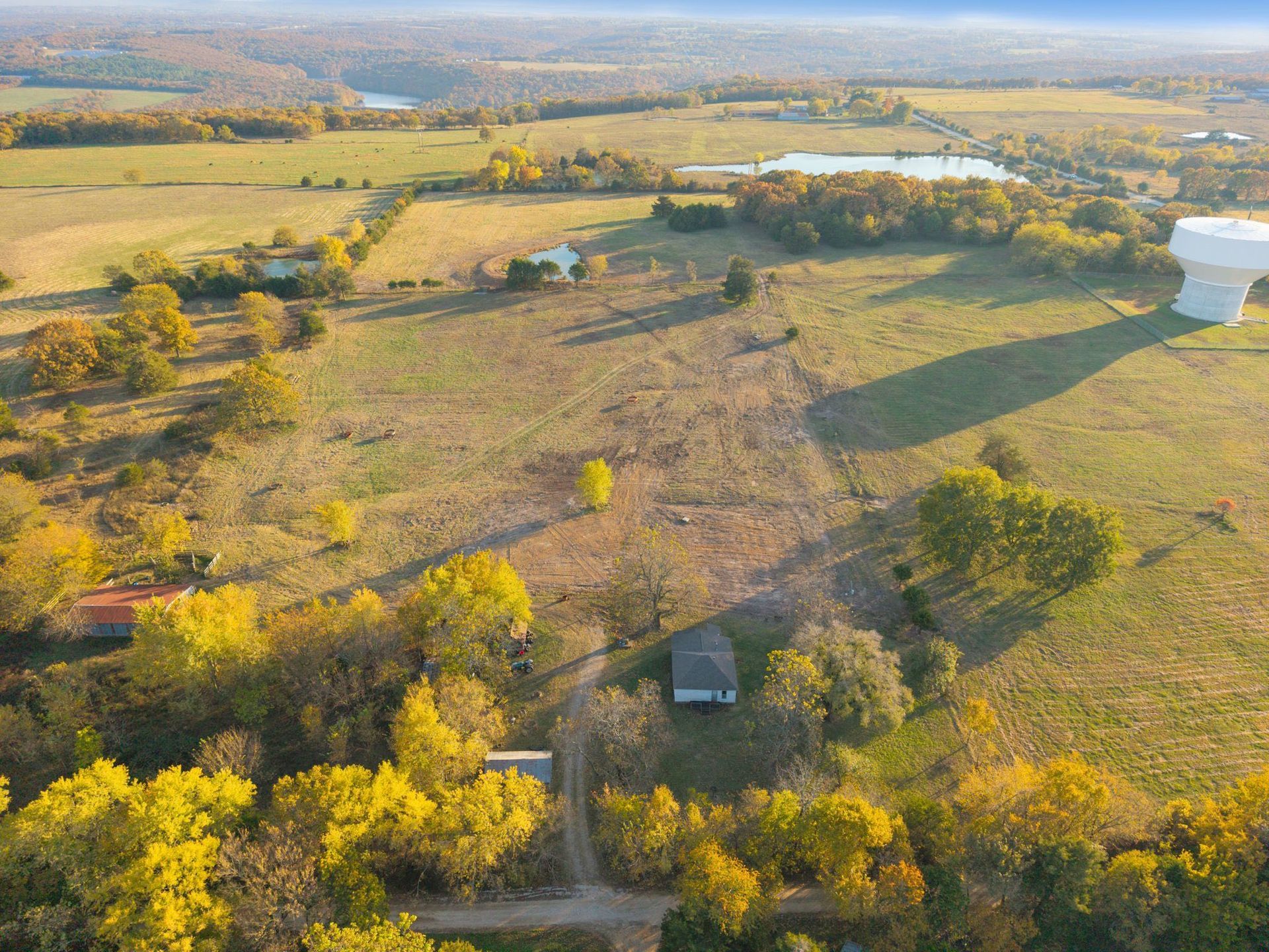 Aerial view of a rural landscape with fields, trees, a house, and a water tower.