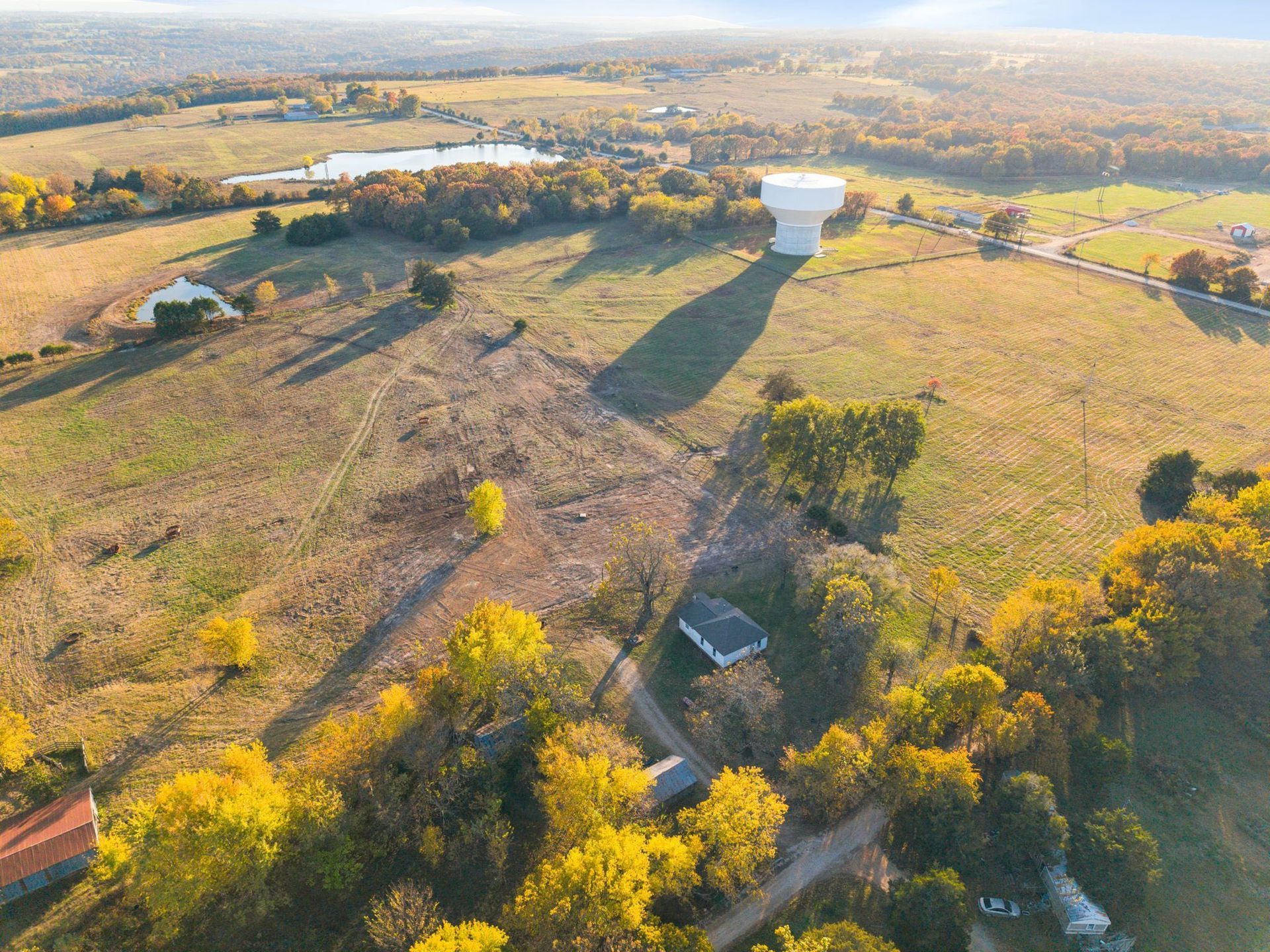 Aerial view of rural landscape with a water tower, a small lake, and fall foliage.