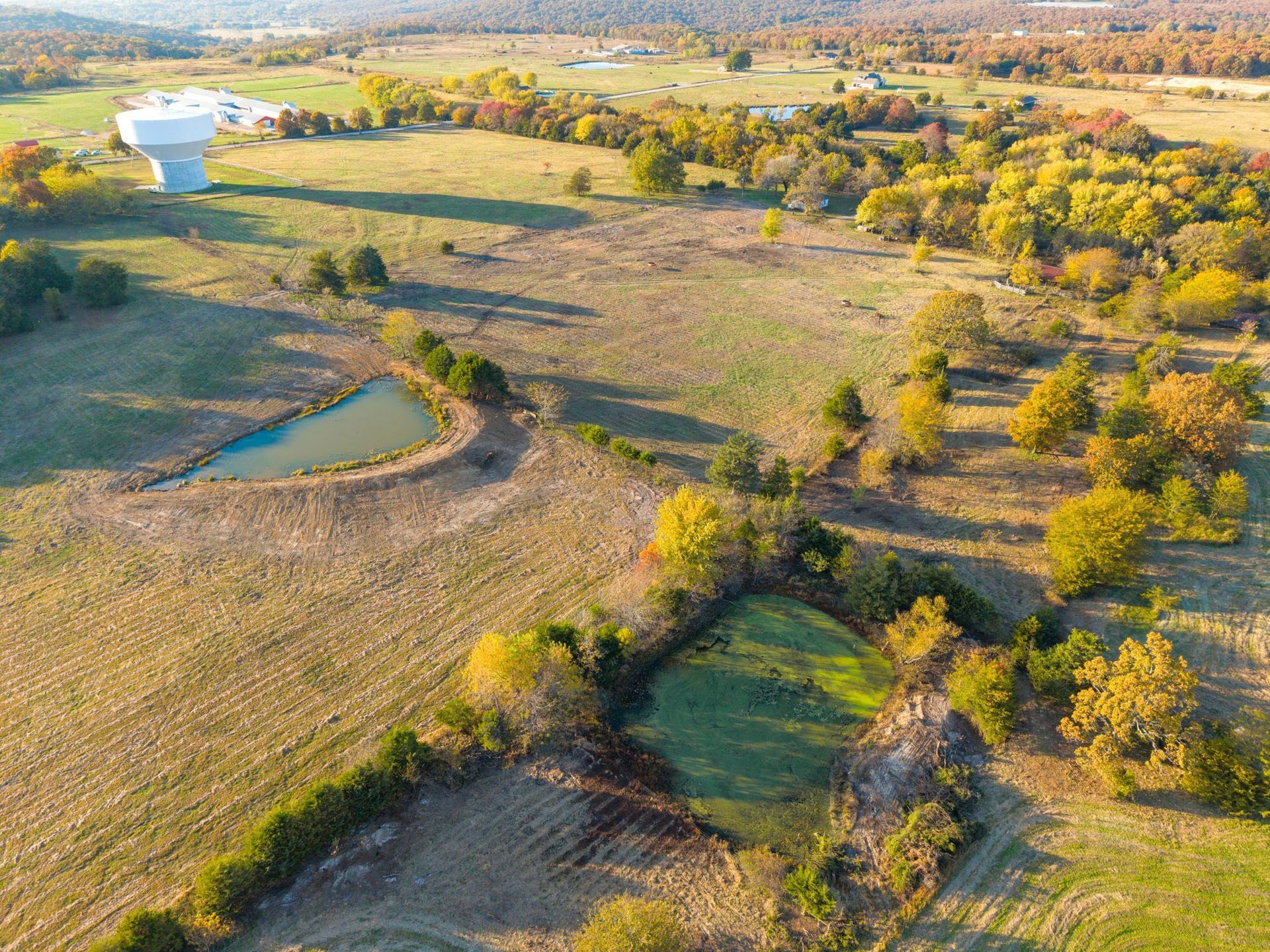 Aerial view of rural landscape with fall foliage, pond, and water tower.