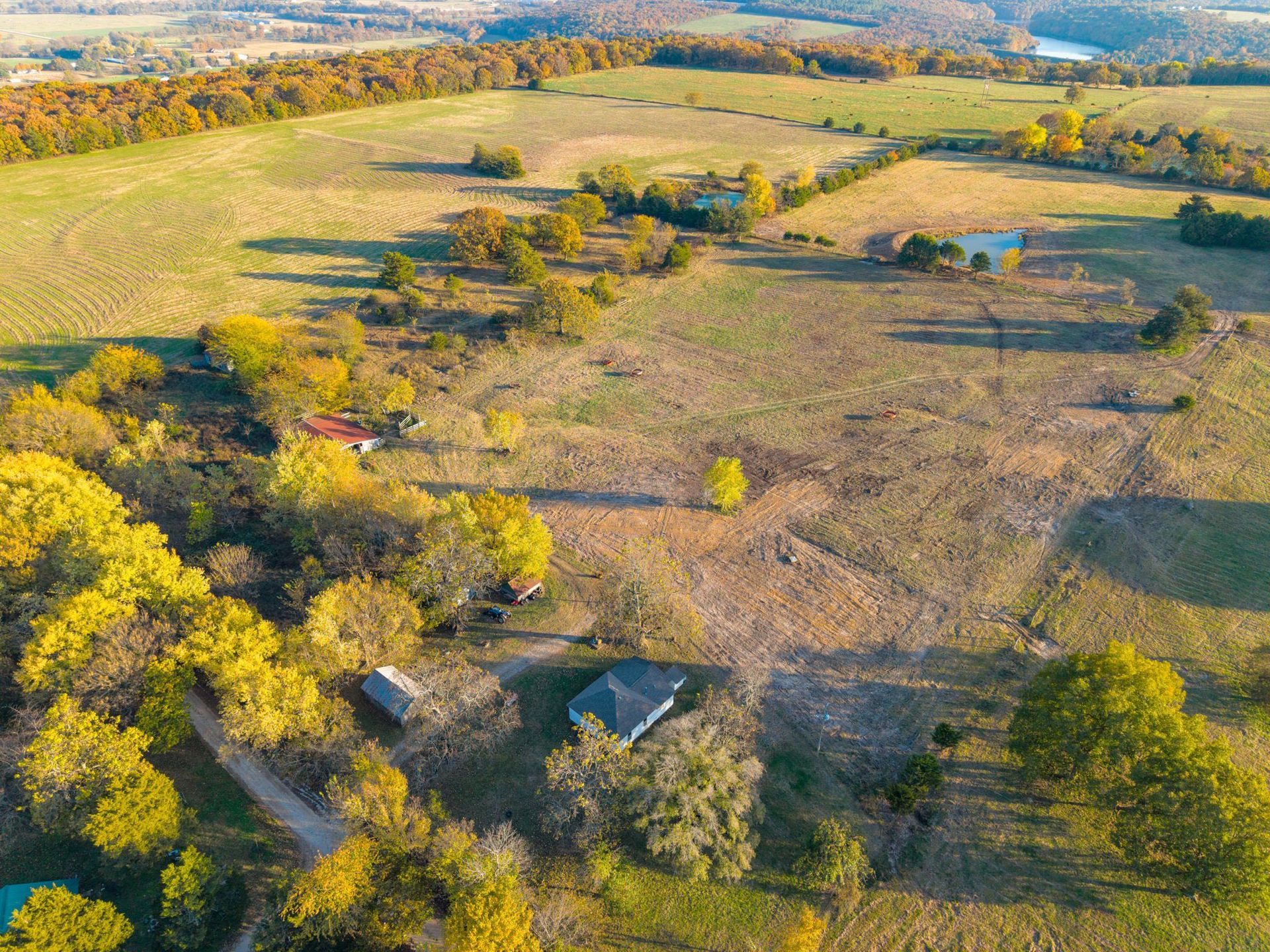 Aerial view of a rural landscape with rolling fields, trees, and small buildings; autumn colors.