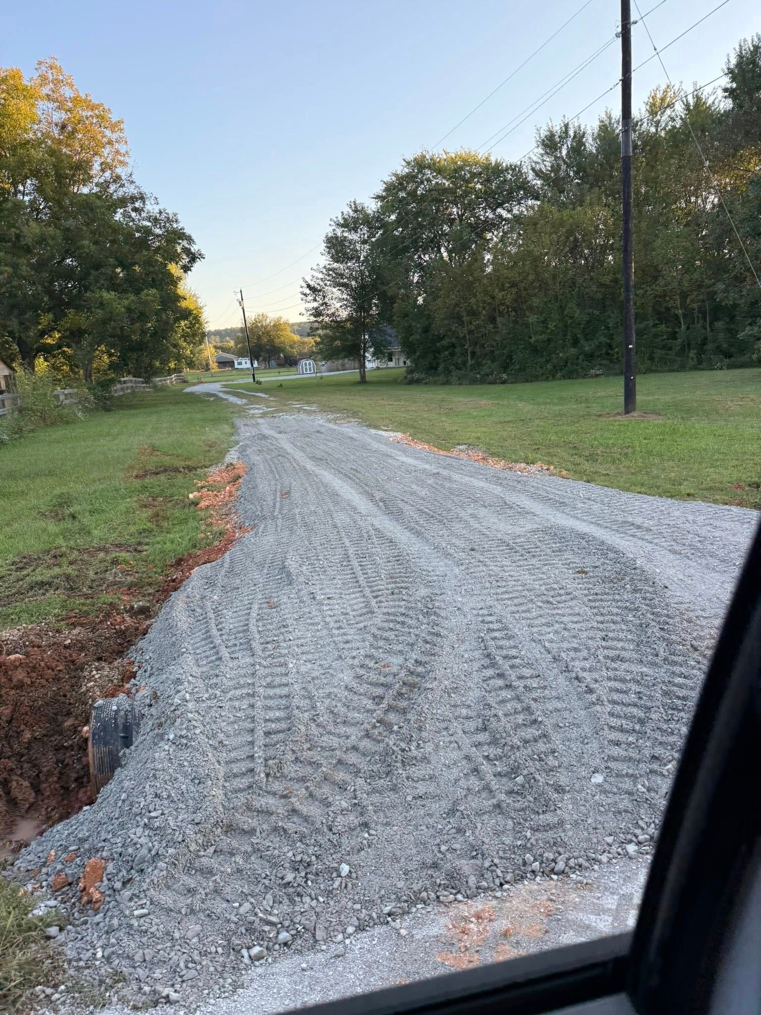 Gravel driveway with tire tracks in grass setting, trees and power lines in the background.