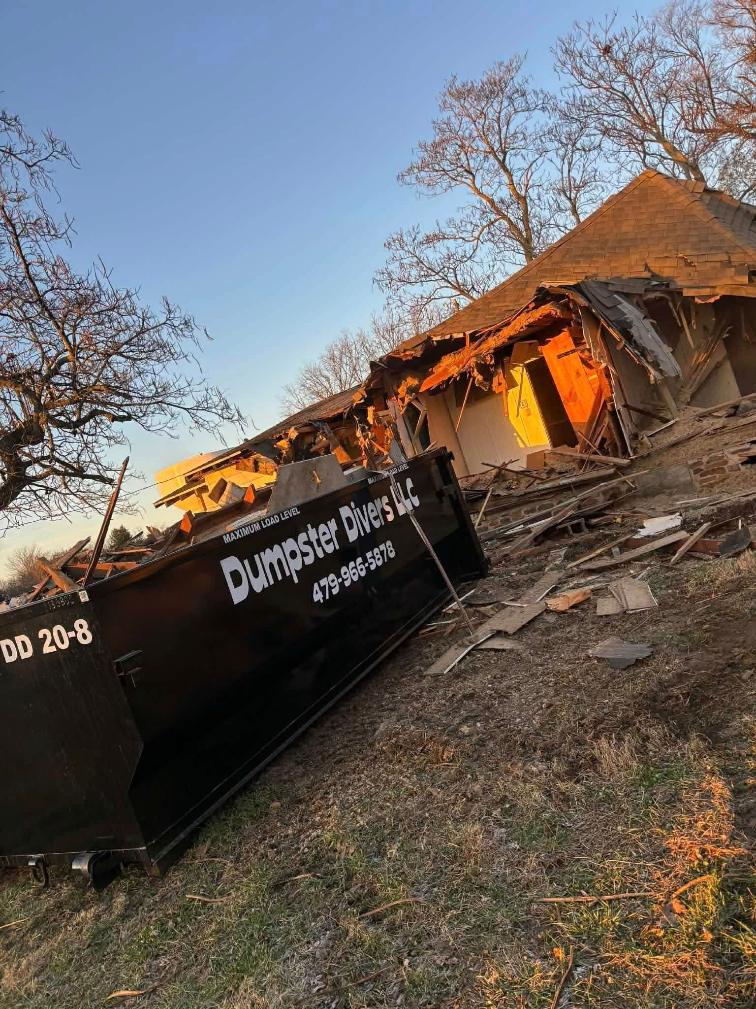Demolished building with a dumpster in front. Debris and exposed structure visible. Overcast, daylight.