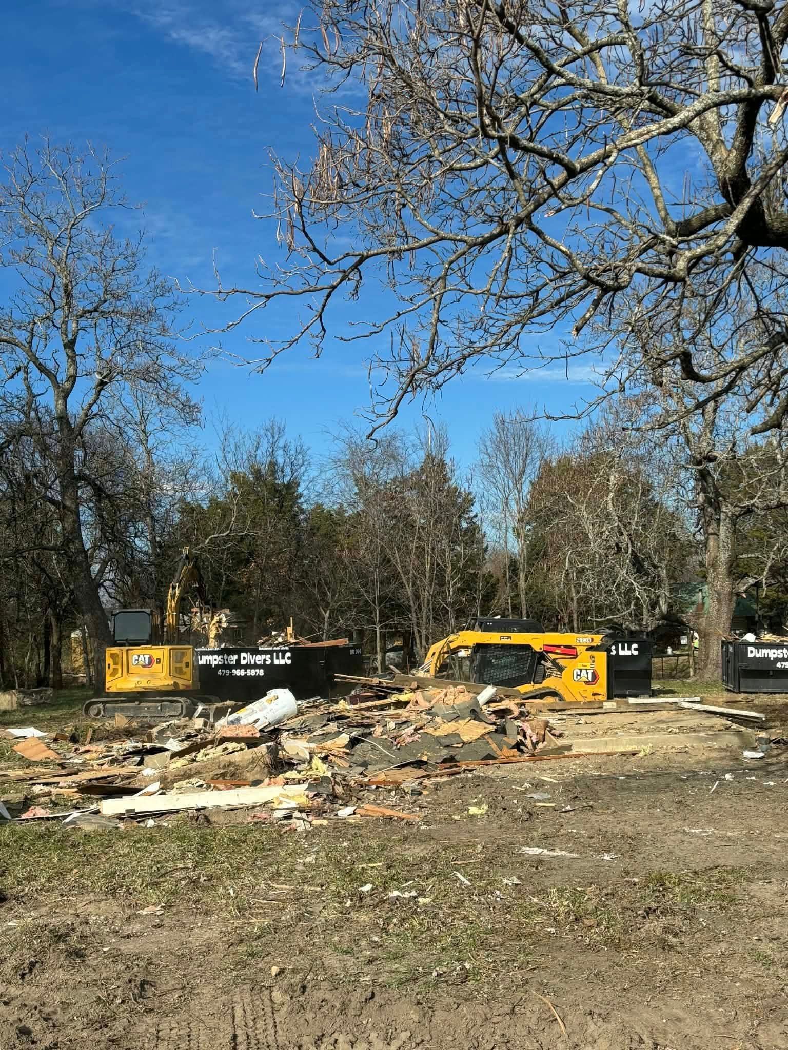 Construction site with two yellow excavators, debris, trees, and a blue sky.