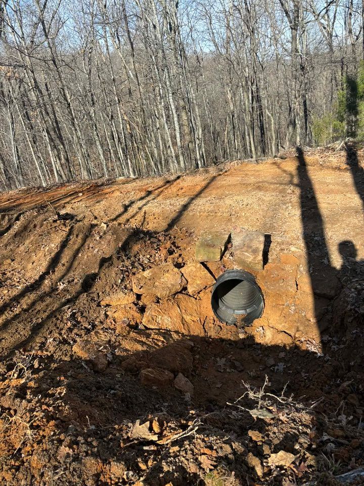 Black culvert pipe in a dirt embankment with bare trees in the background.