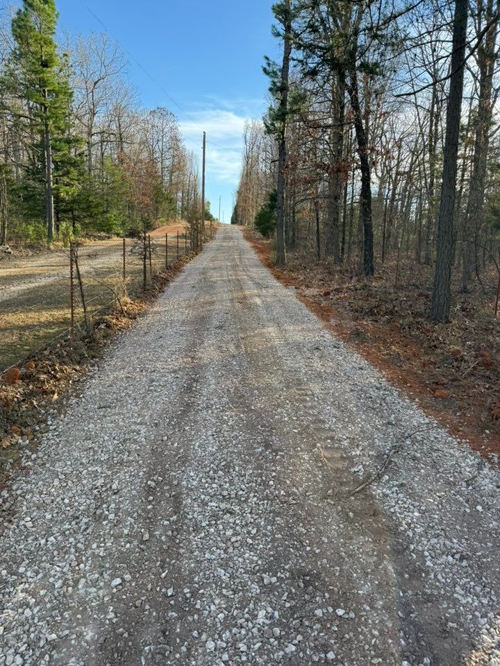 Gravel road lined by trees stretches into the distance under a blue sky.
