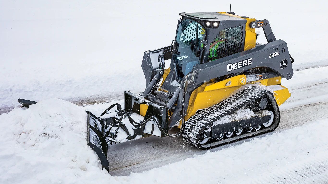 Yellow John Deere skid steer with snow blower clearing snow.
