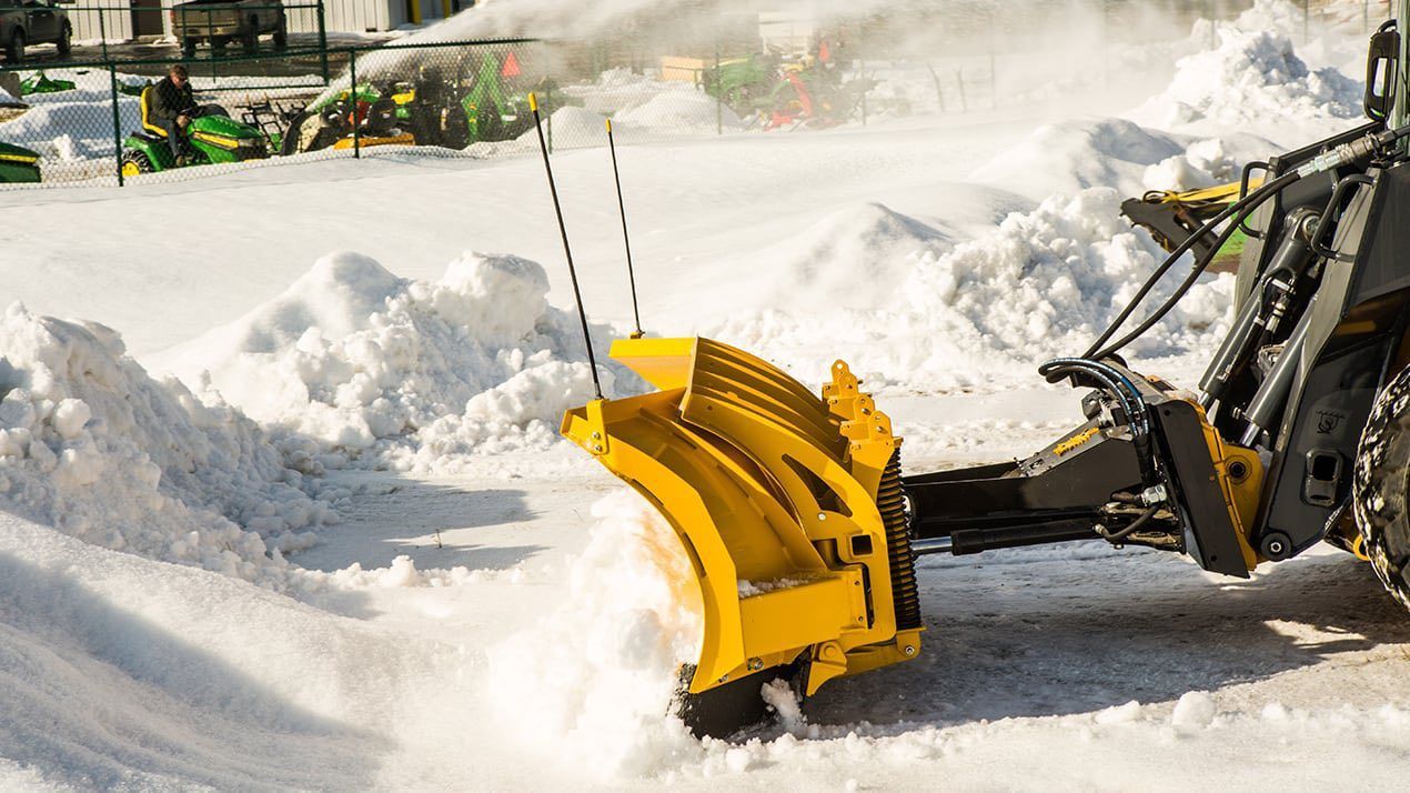 Yellow snowplow clearing snow on a bright, sunny day.