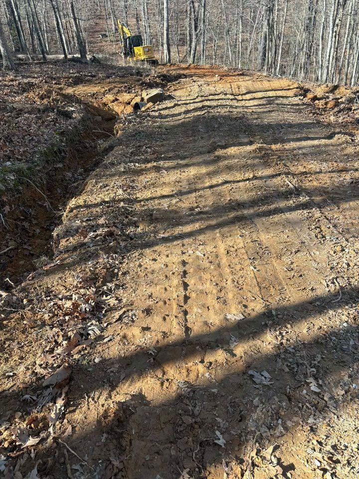 Dirt path with excavator digging a trench in a wooded area.
