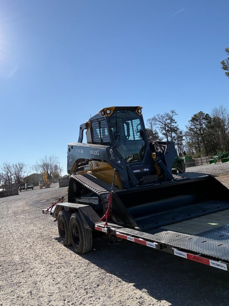 Skid steer loader on a trailer in a sunny, outdoor setting.