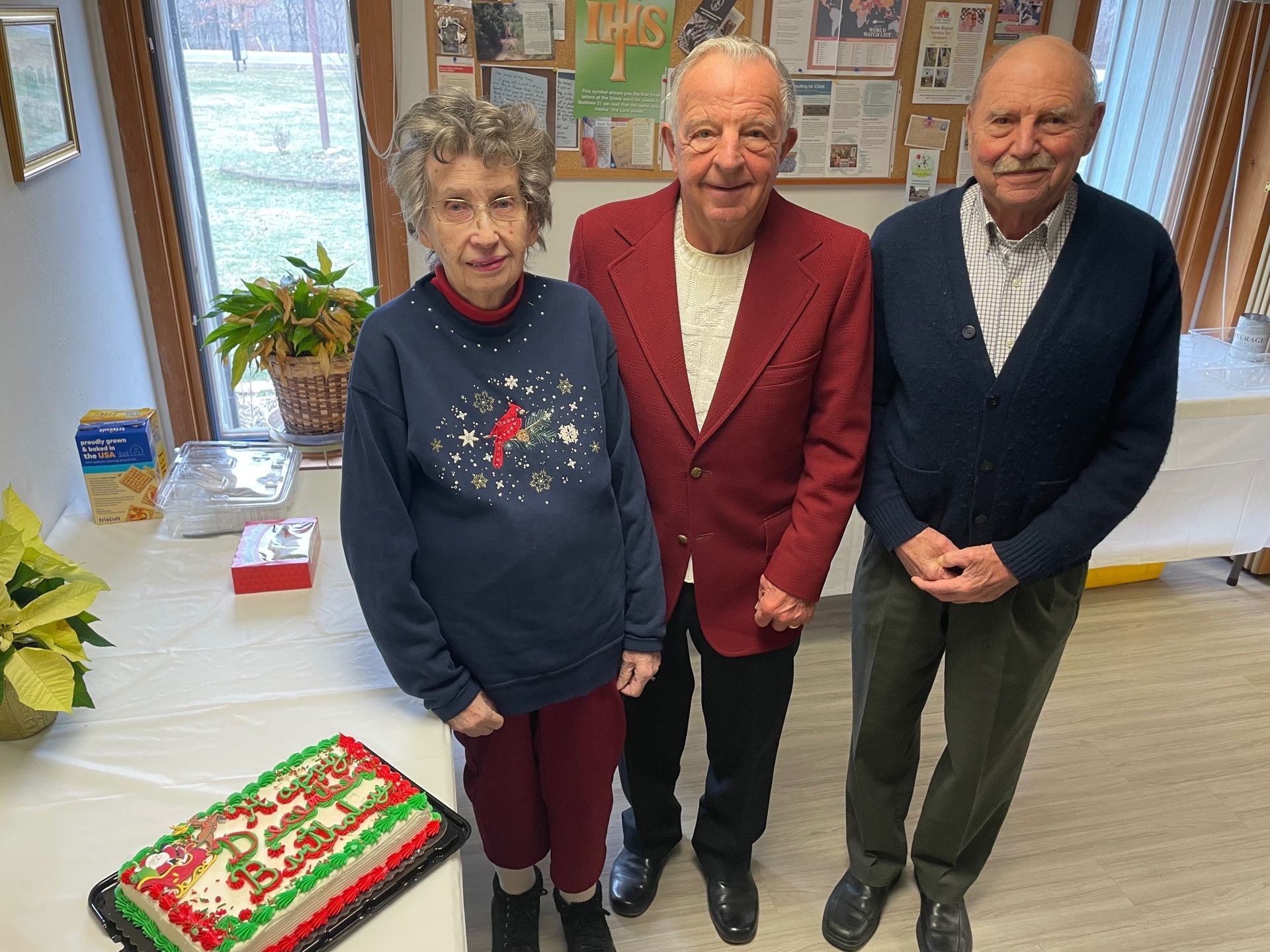 Three people are standing in front of a christmas cake.