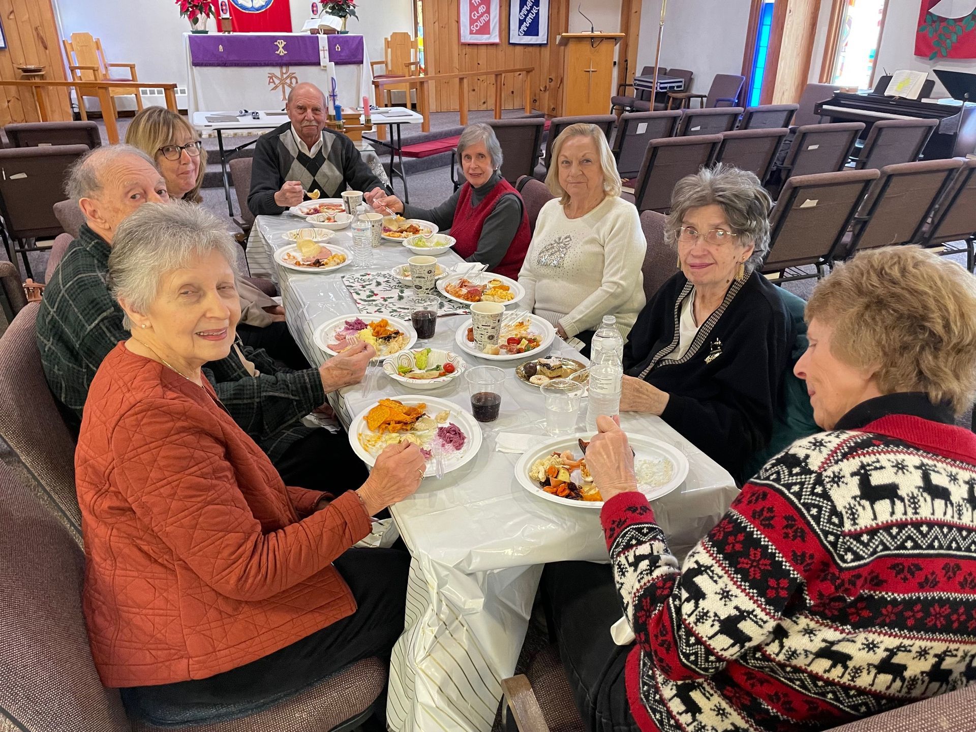 A group of elderly people are sitting around a long table eating food.