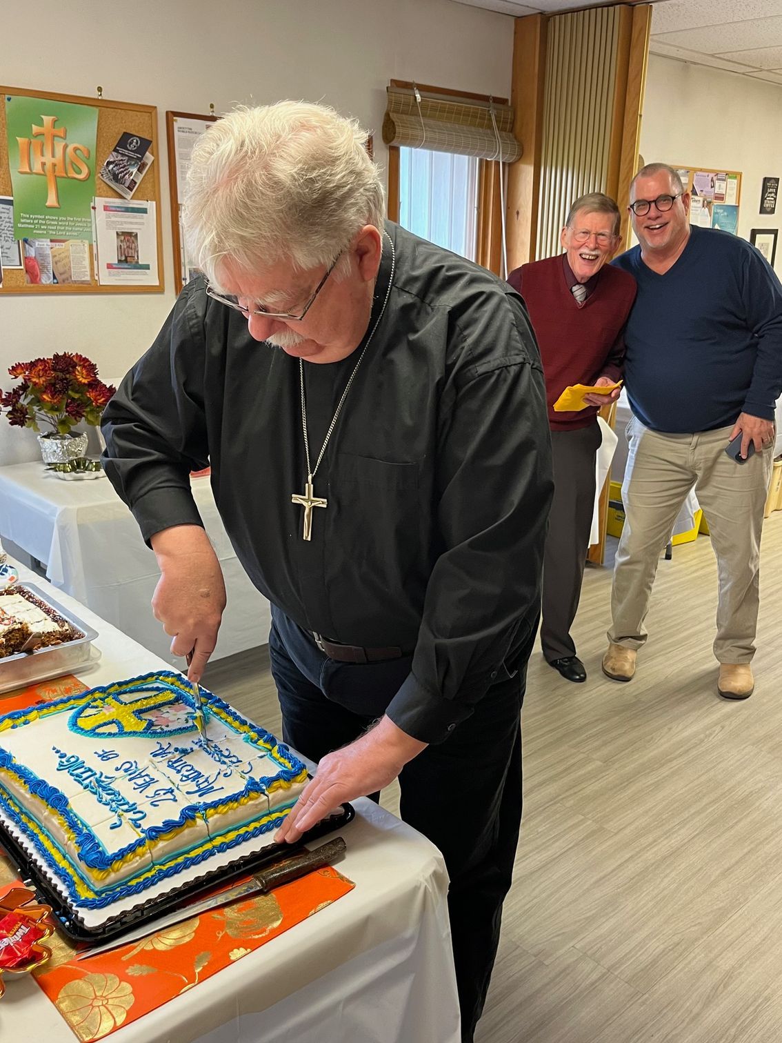 A man in a black shirt is cutting a cake on a table.