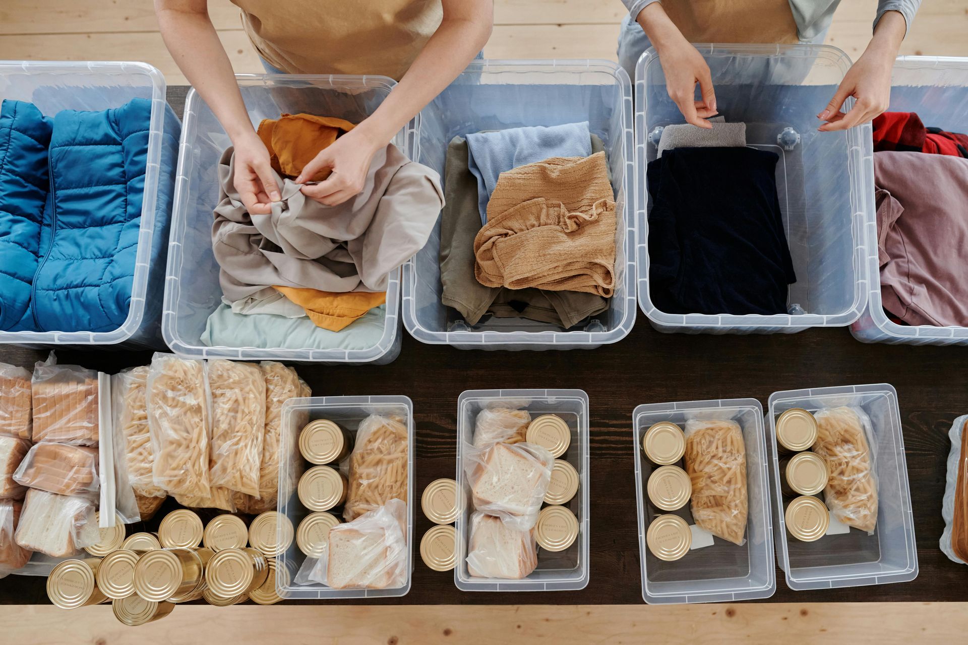 Two people are sorting clothes in plastic bins on a table.