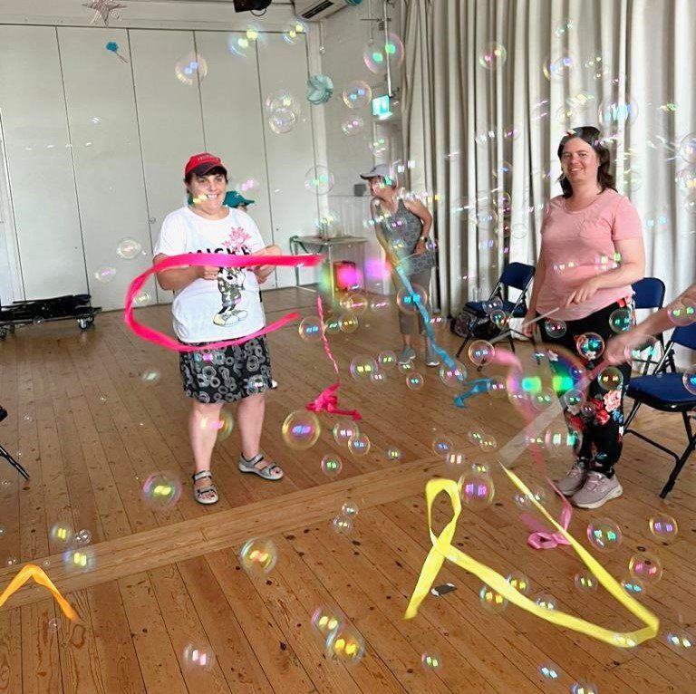 At Ashcroft Arts Centre smiling FNC members move ribbons to music and through many bubbles floating in the air produced by a bubble machine