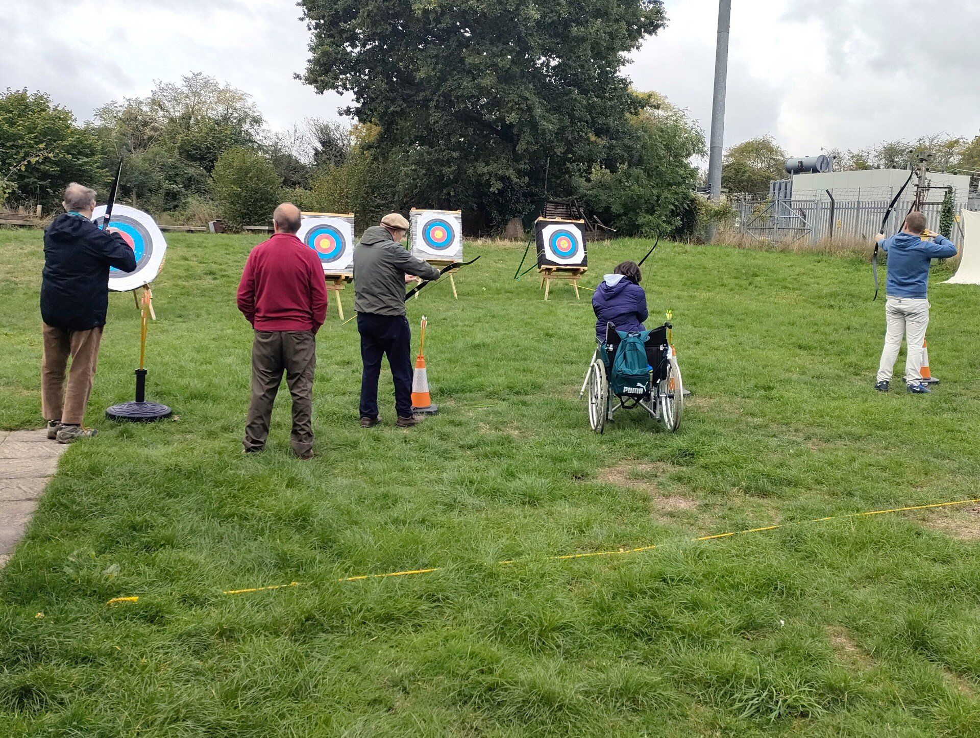 Outside in the filed: FNC members including one in wheelchair, with volunteer archery instructor, take aim at  archery targets