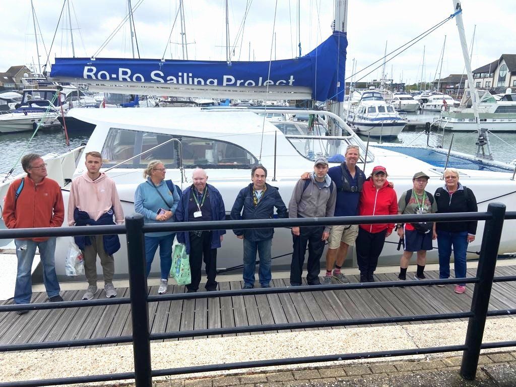 Members and volunteers stand on a jetty in front of the 'Ro Ro Project' white hulled accessible catamaran