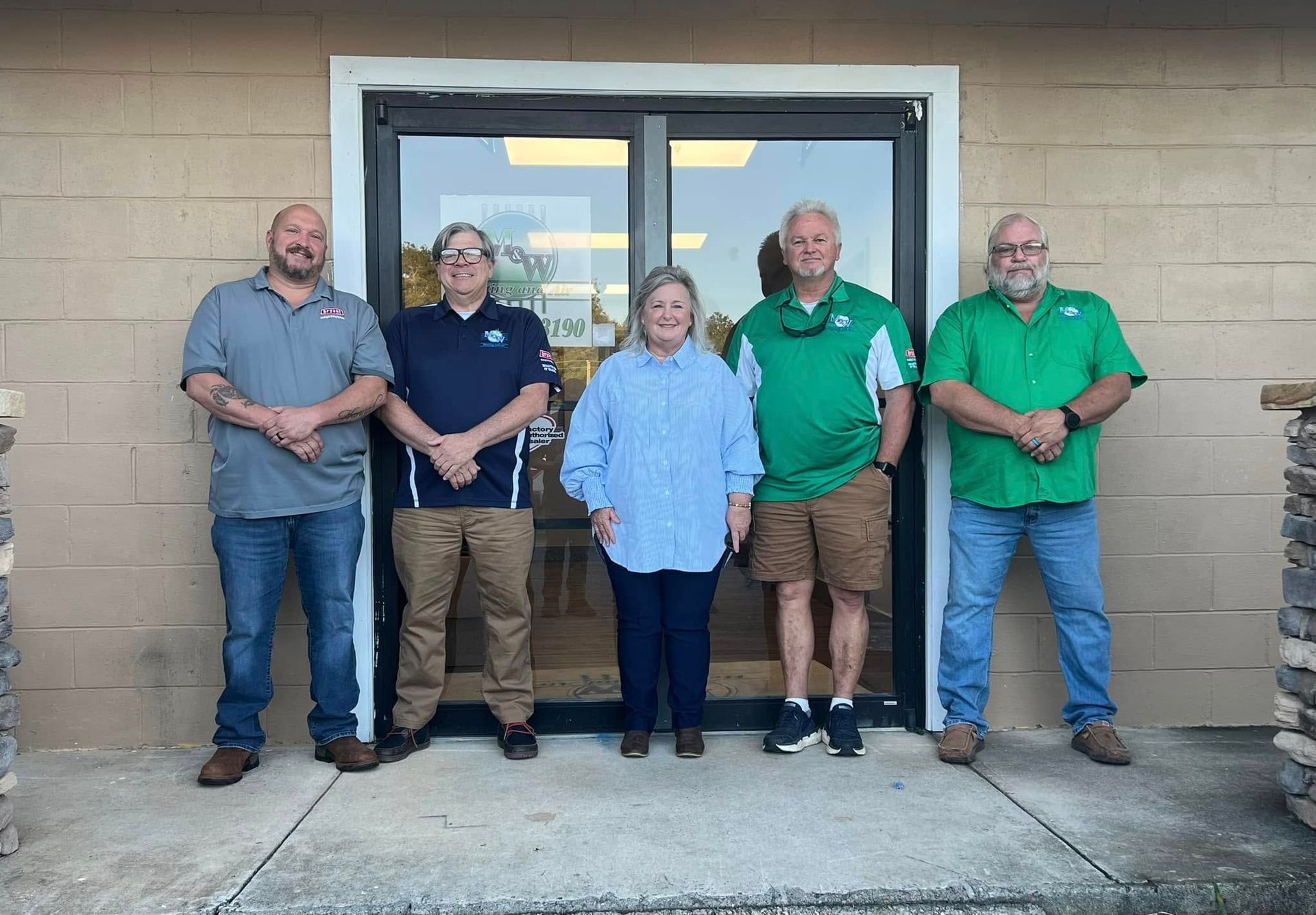 Five people standing in front of a glass door. They are wearing casual clothes. A building with stone pillars is behind them.