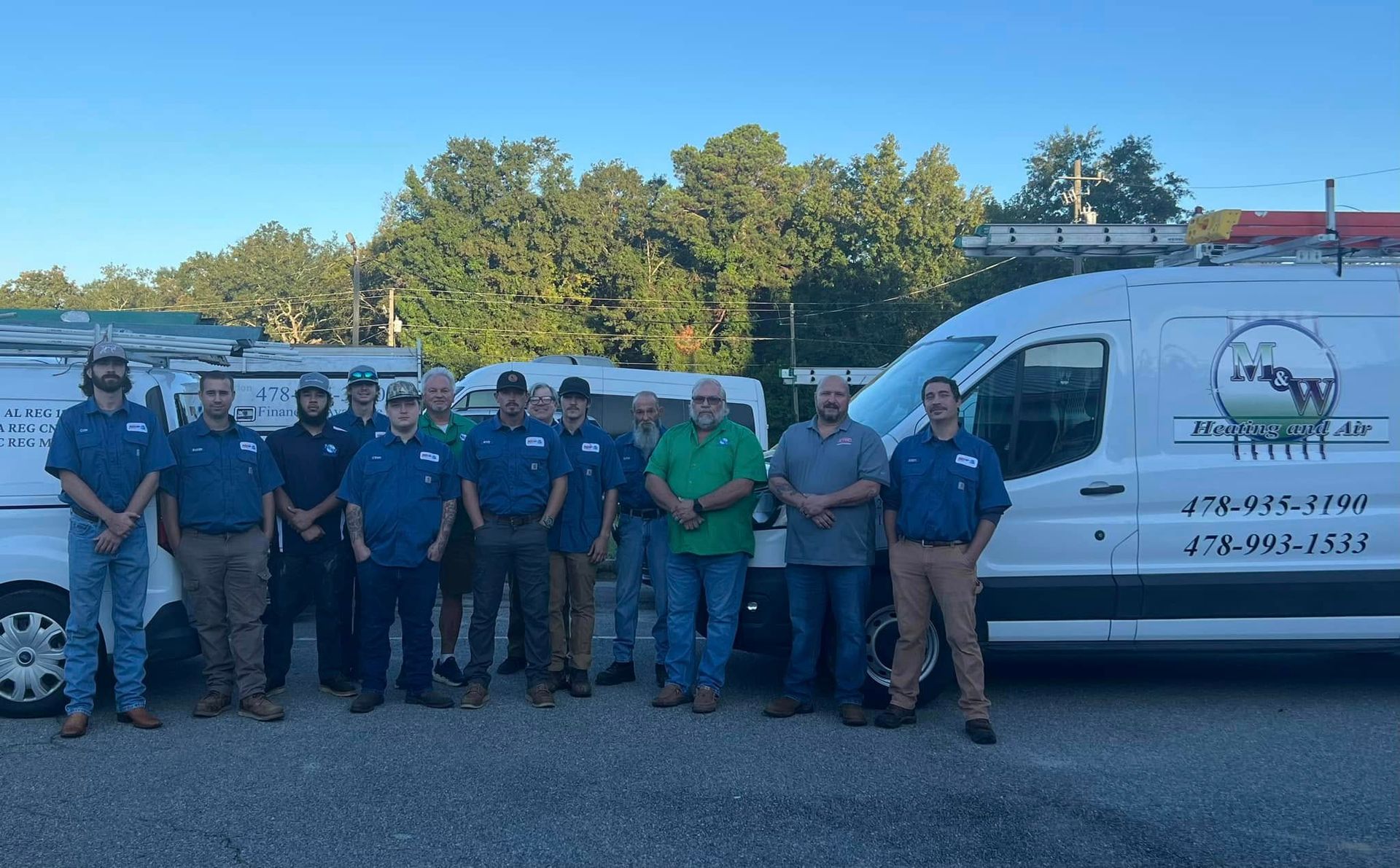Group of men in work shirts pose with company vans.