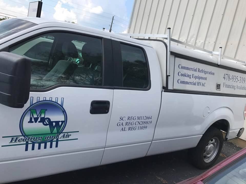 White work truck with company logo and contact info parked in front of a building.