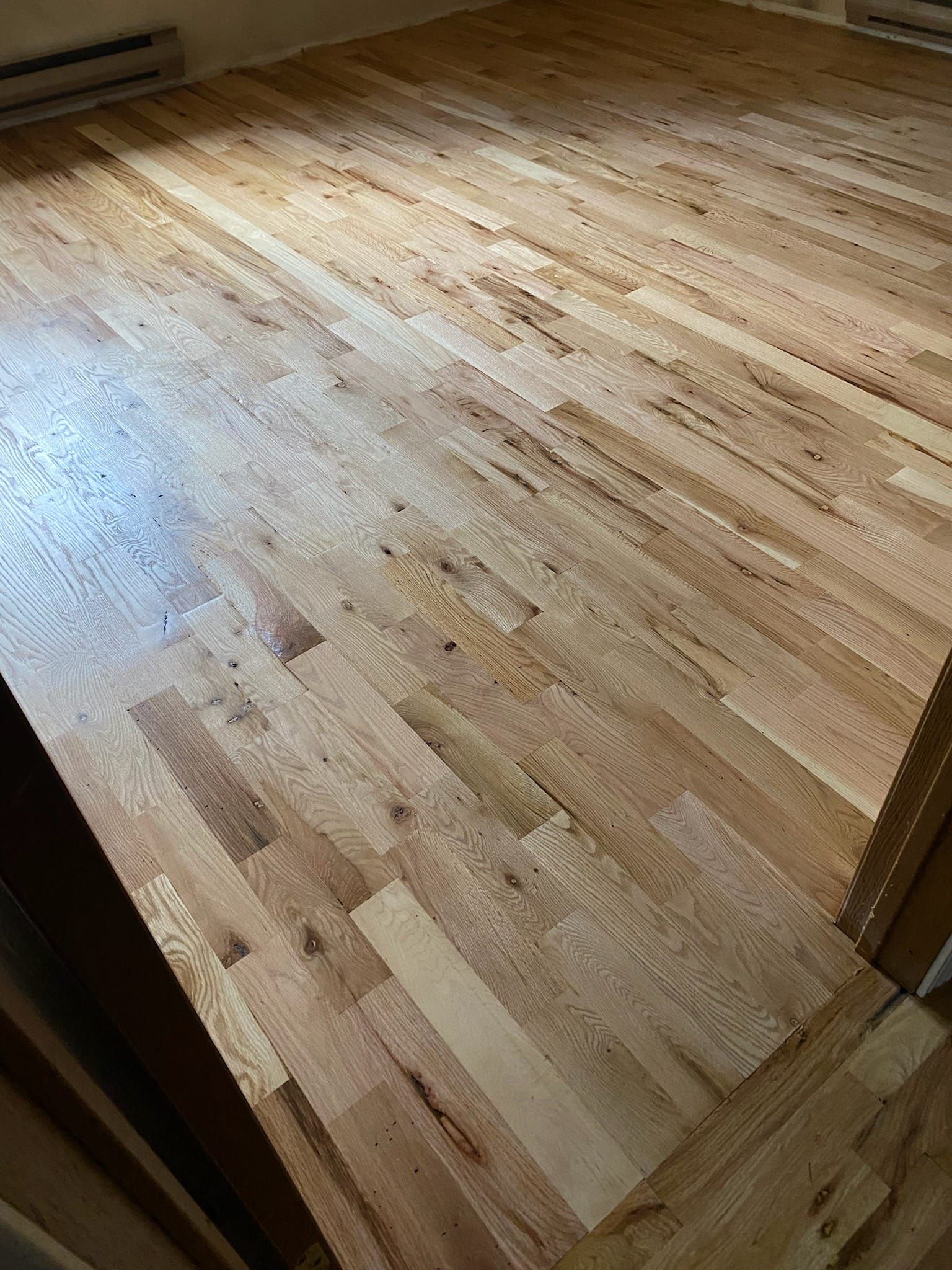Wooden hardwood flooring, diagonally installed, bathed in sunlight.