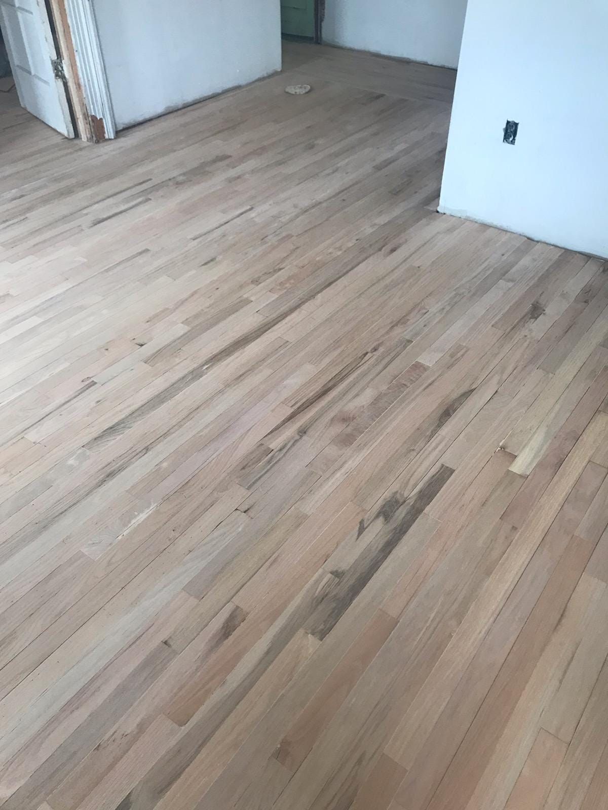 Light-colored, unfinished hardwood floor in a room with white walls.
