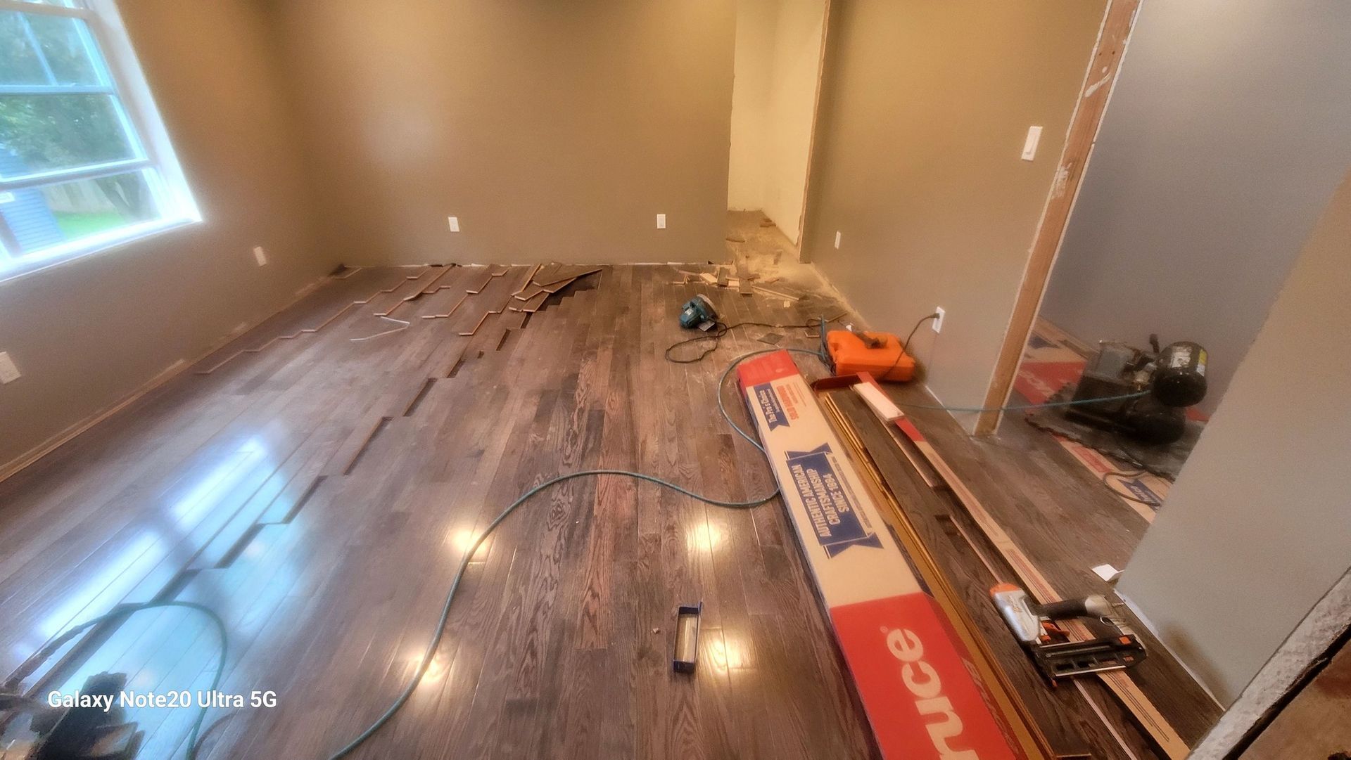 Room with partially installed brown wood flooring, tools, and a doorway.