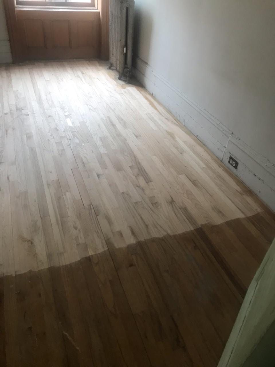Bare hardwood floor, partly sanded, in a room with light walls and a window.