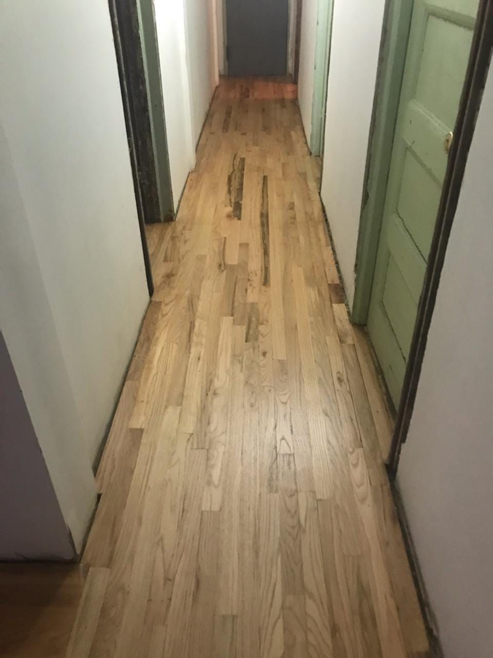 Narrow hallway with light-colored wood floor, two doors, and off-white walls.