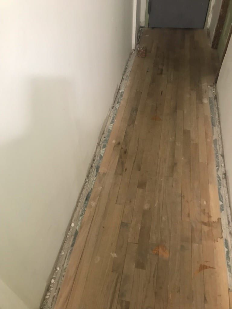 Narrow hallway with hardwood floor, bare along the walls, between white walls.