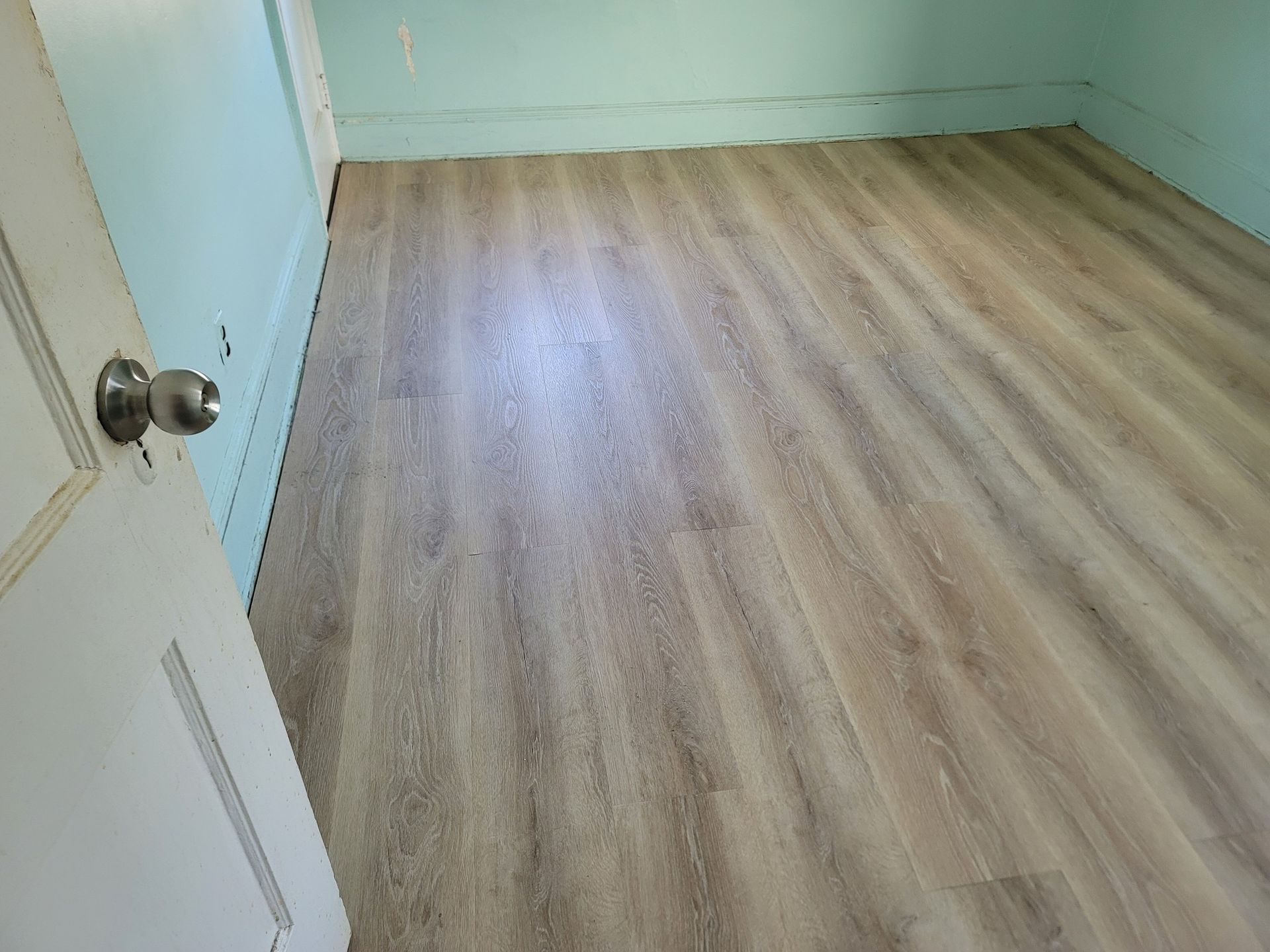 Room with wood-look flooring and blue walls. A white door with a doorknob is on the left.