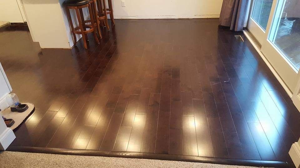 Dark wood floor with glossy finish, transition strip at edge. Bar stools in background.