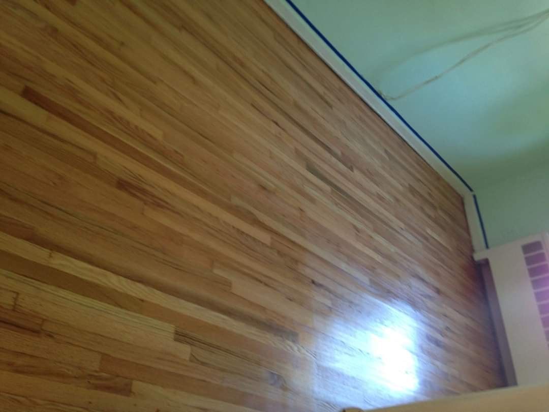 Wooden wall paneling with blue tape at the ceiling, adjacent to a light-green wall and a pink trim.