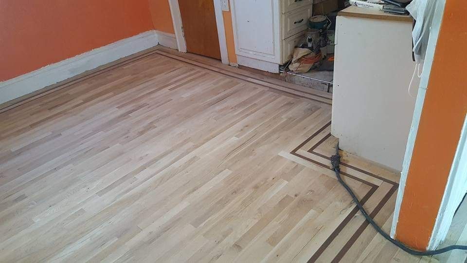 Hardwood flooring installation with dark border, orange walls, and doorway.