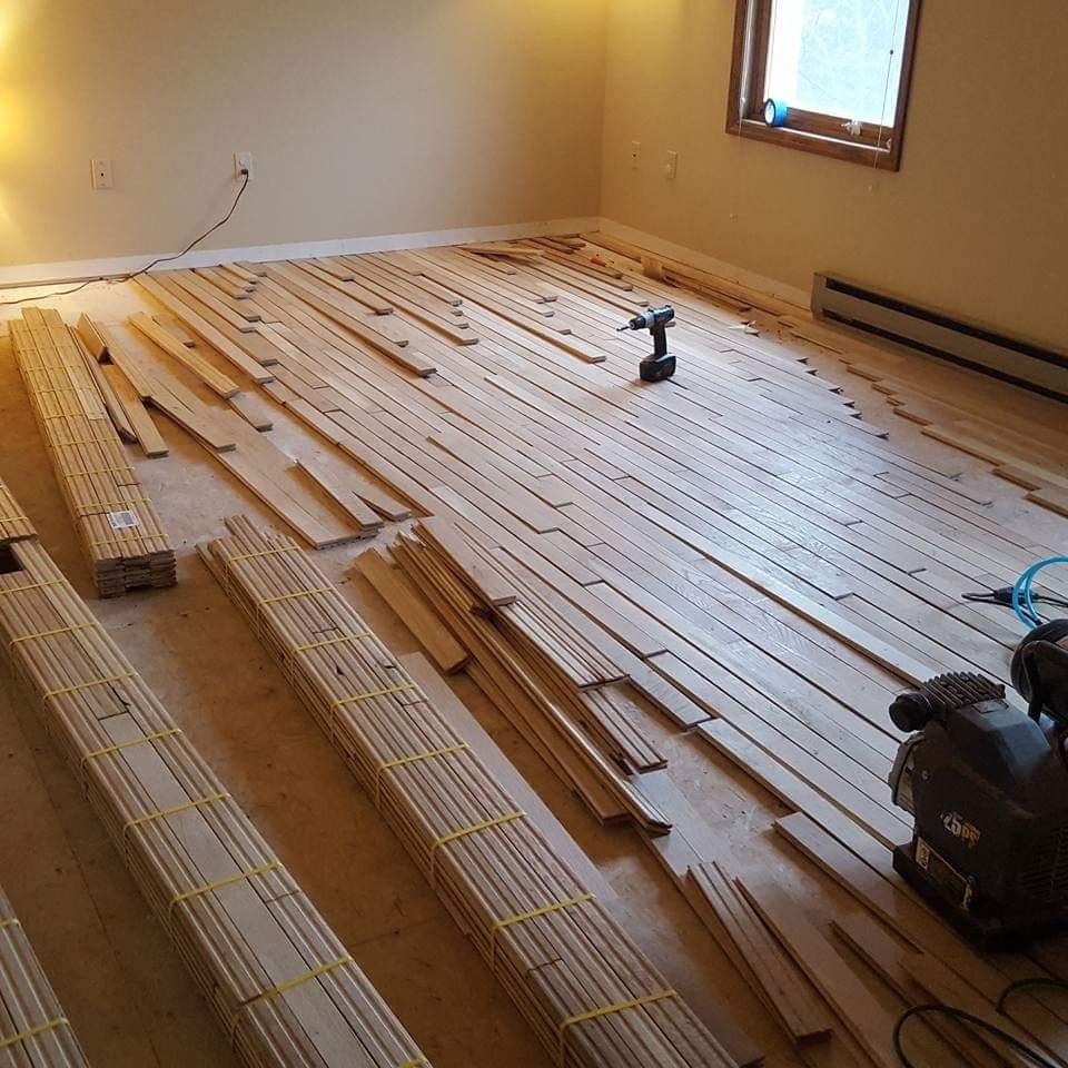 Wooden floorboards being installed in a room. Bundles of boards lie on the floor beside a drill and air compressor.
