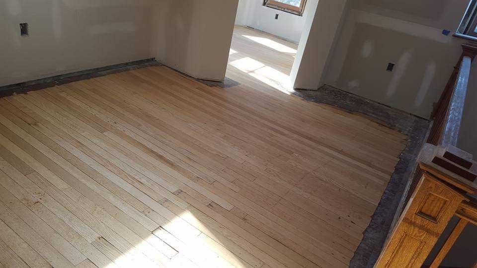 Light-colored hardwood floor in a room under construction. Walls are unpainted, doorway leads to another room.