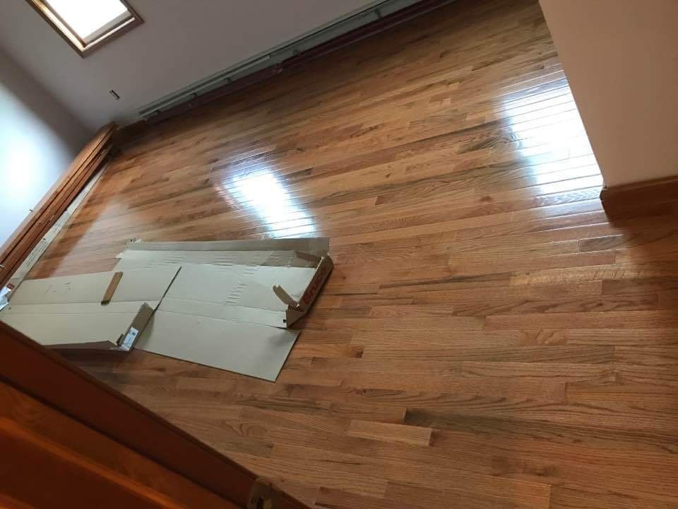 Hardwood floor with scattered cardboard boxes, likely newly installed. Sunlit, warm tones.