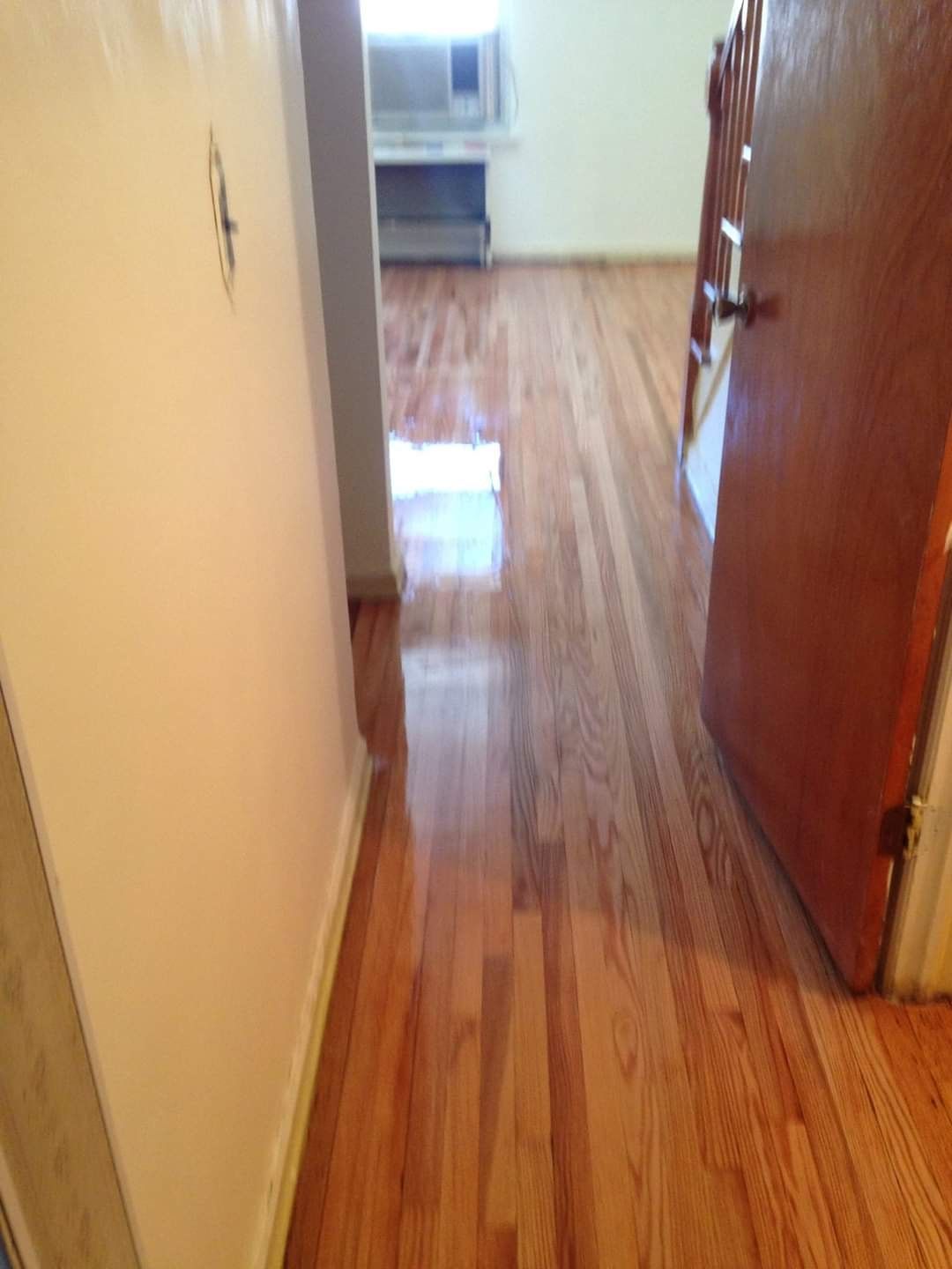 Wooden floor hallway with a door, leading to a room with an air conditioner.