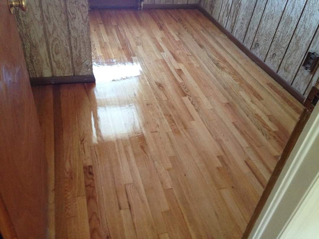 Shiny wooden floor in a room, reflecting light. Walls are wood paneling.